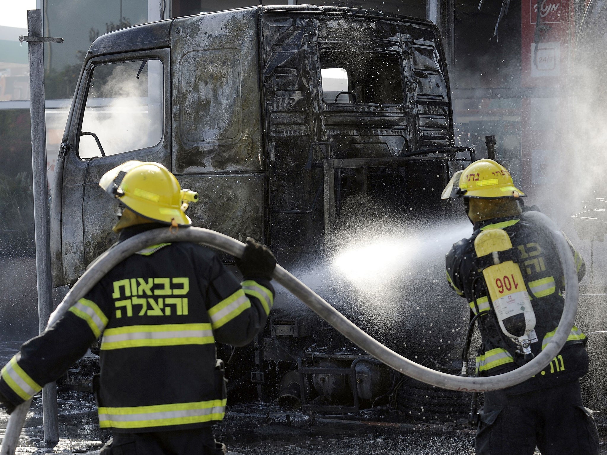 Israeli fire fighters extinguish vehicles destroyed by a rocket fired from the Gaza Strip in the city of Ashdod