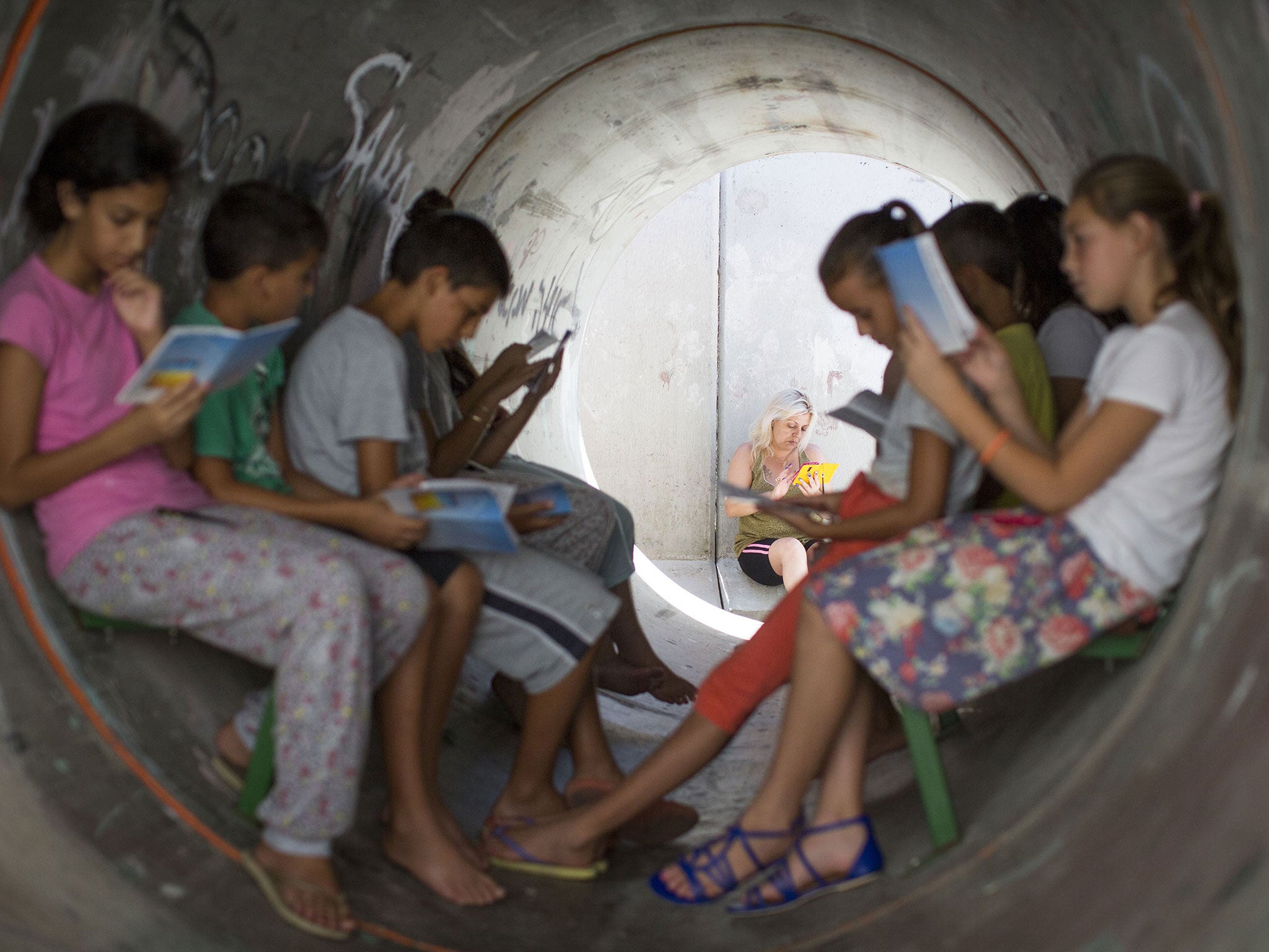 Children read while sitting in a street shelter, in anticipation of Code Red sirens alerting of incoming rockets