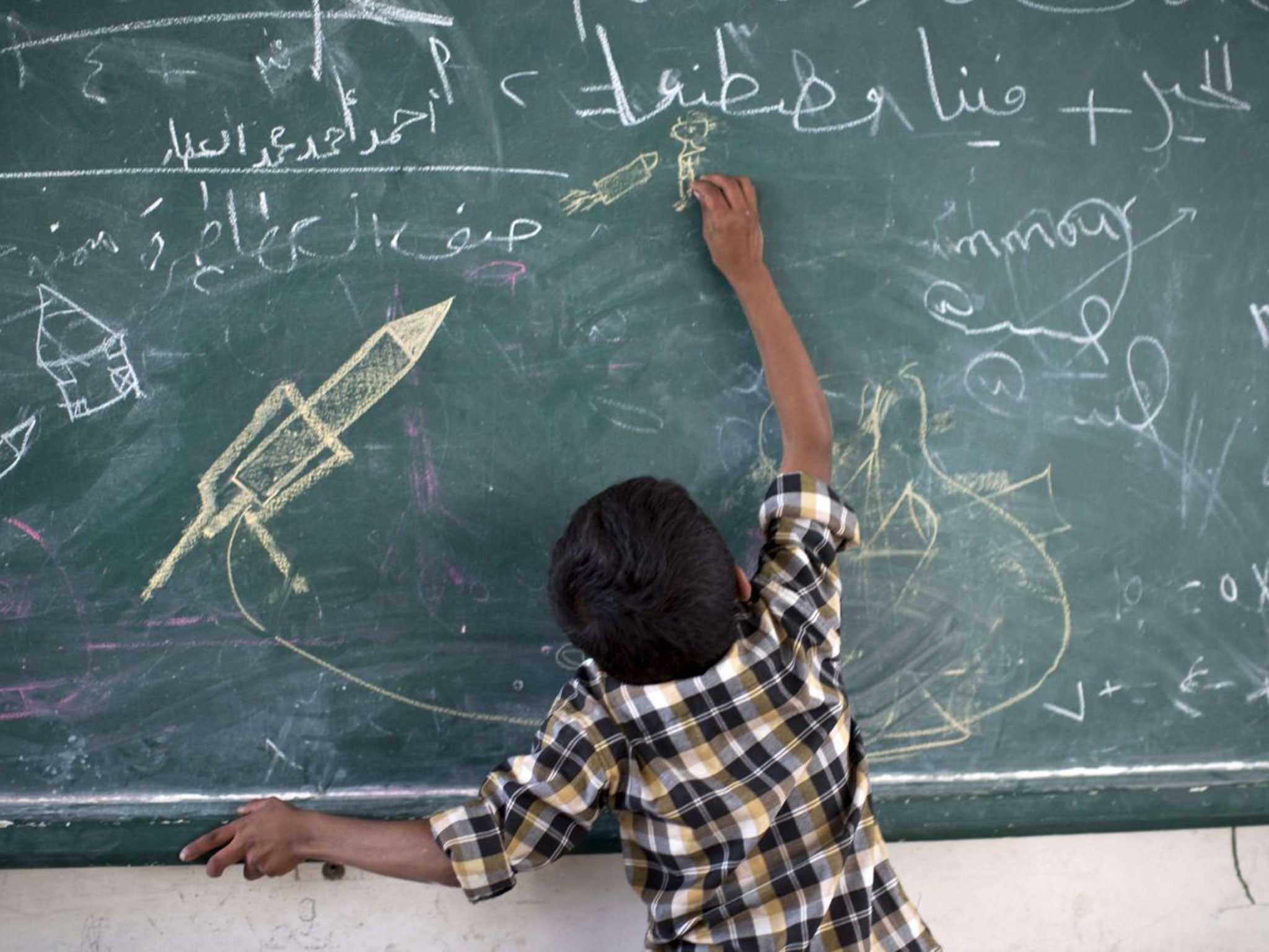 A Palestinian boy draws on the board after fleeing his home