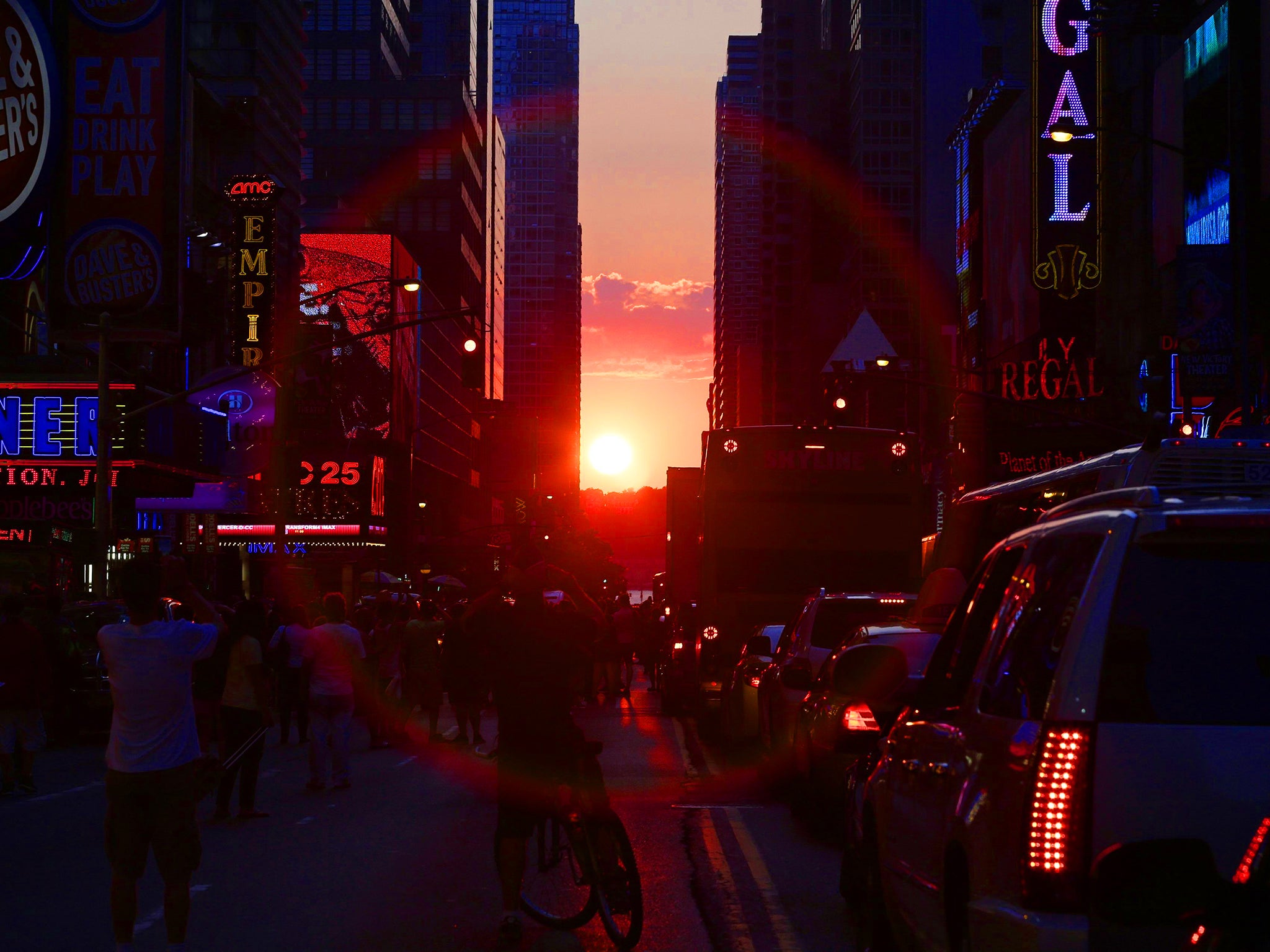 The sun is seen setting behind buildings in Times Square during the Manhattanhenge