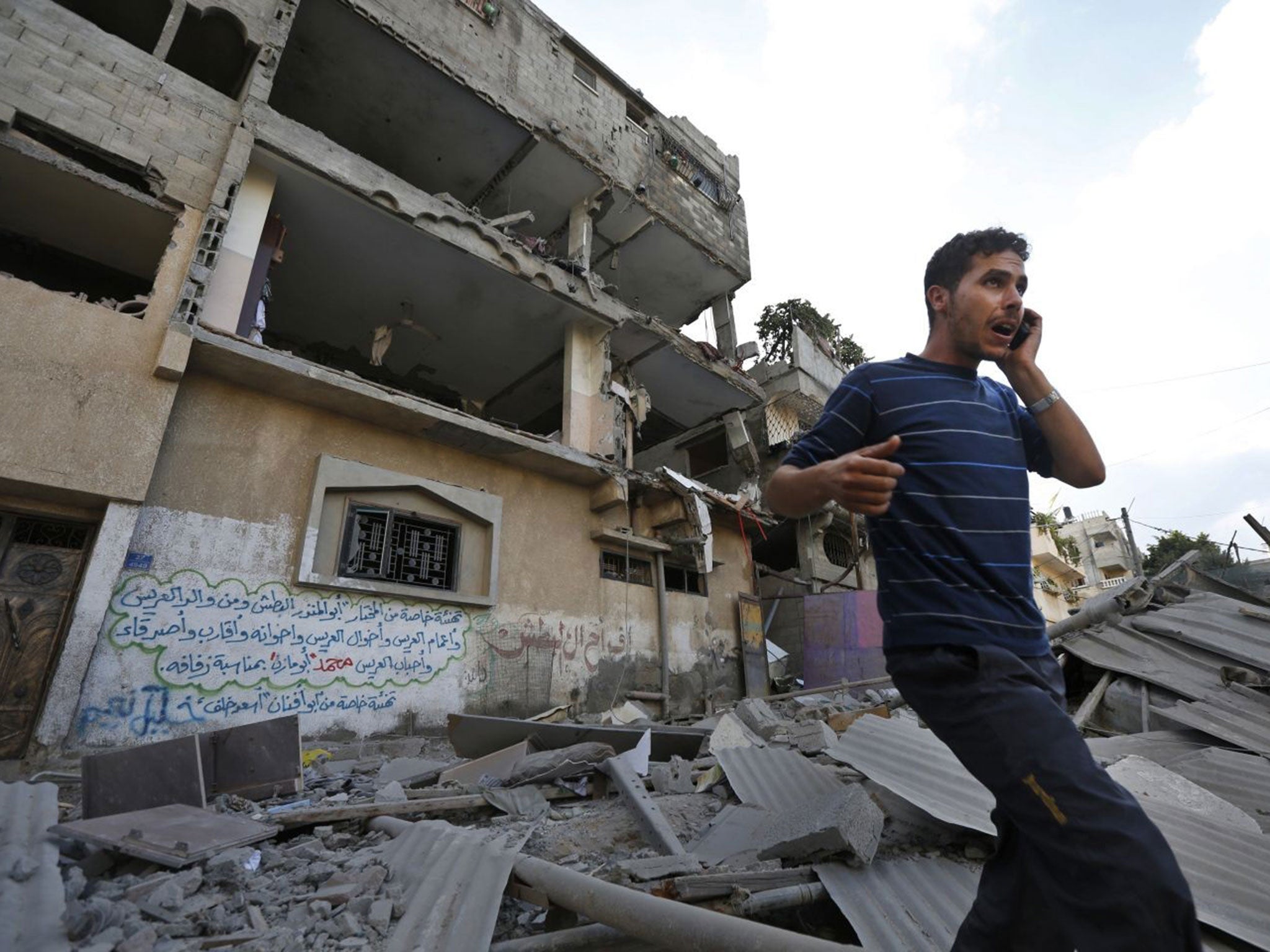 A Palestinian talks on a mobile phone as he walks on the rubble of a damaged house following an overnight Israeli missile strike in Gaza City, Tuesday, July 15, 2014
