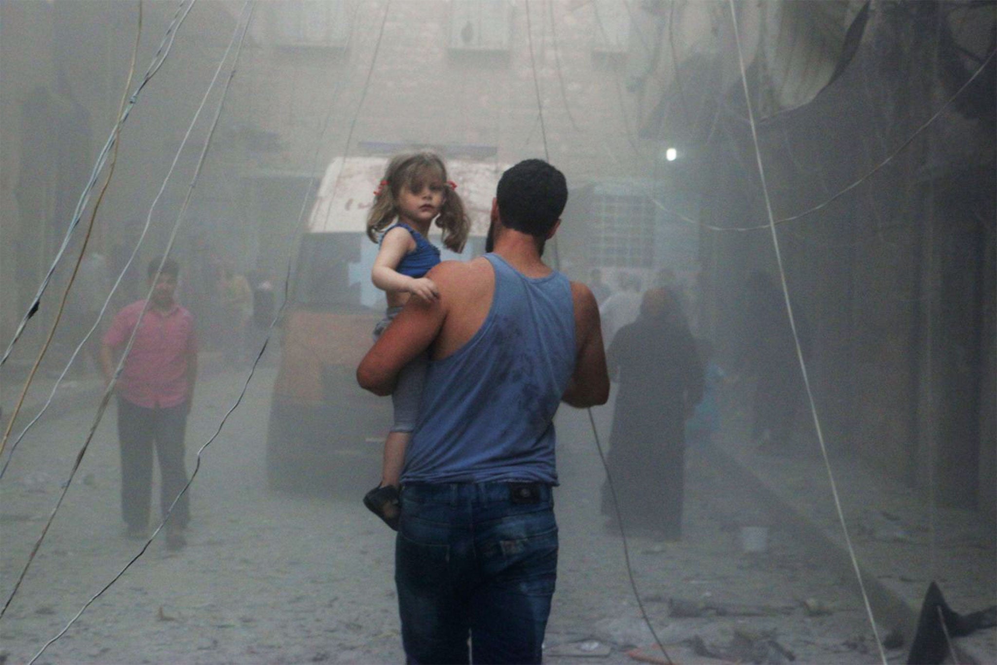 A Syrian man carries a girl on a street covered with dust following an air strike by government forces in the northern city of Aleppo
