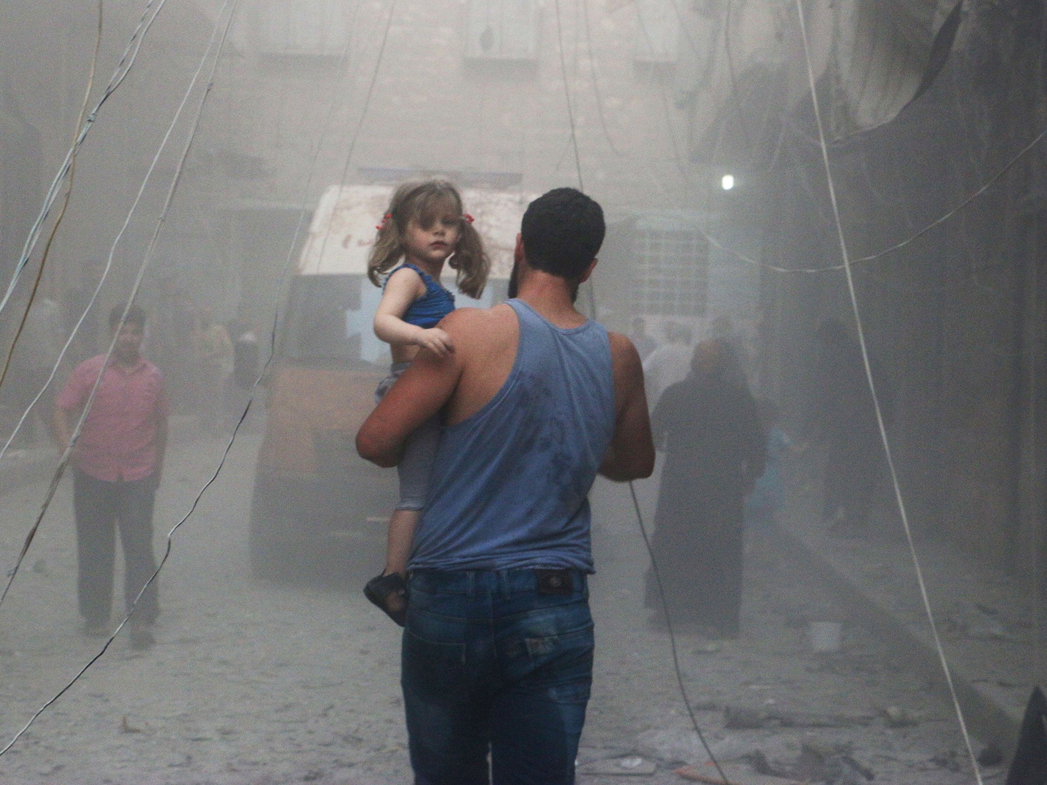 A Syrian man carries a girl on a street covered with dust following a air strike by government forces in the northern city of Aleppo