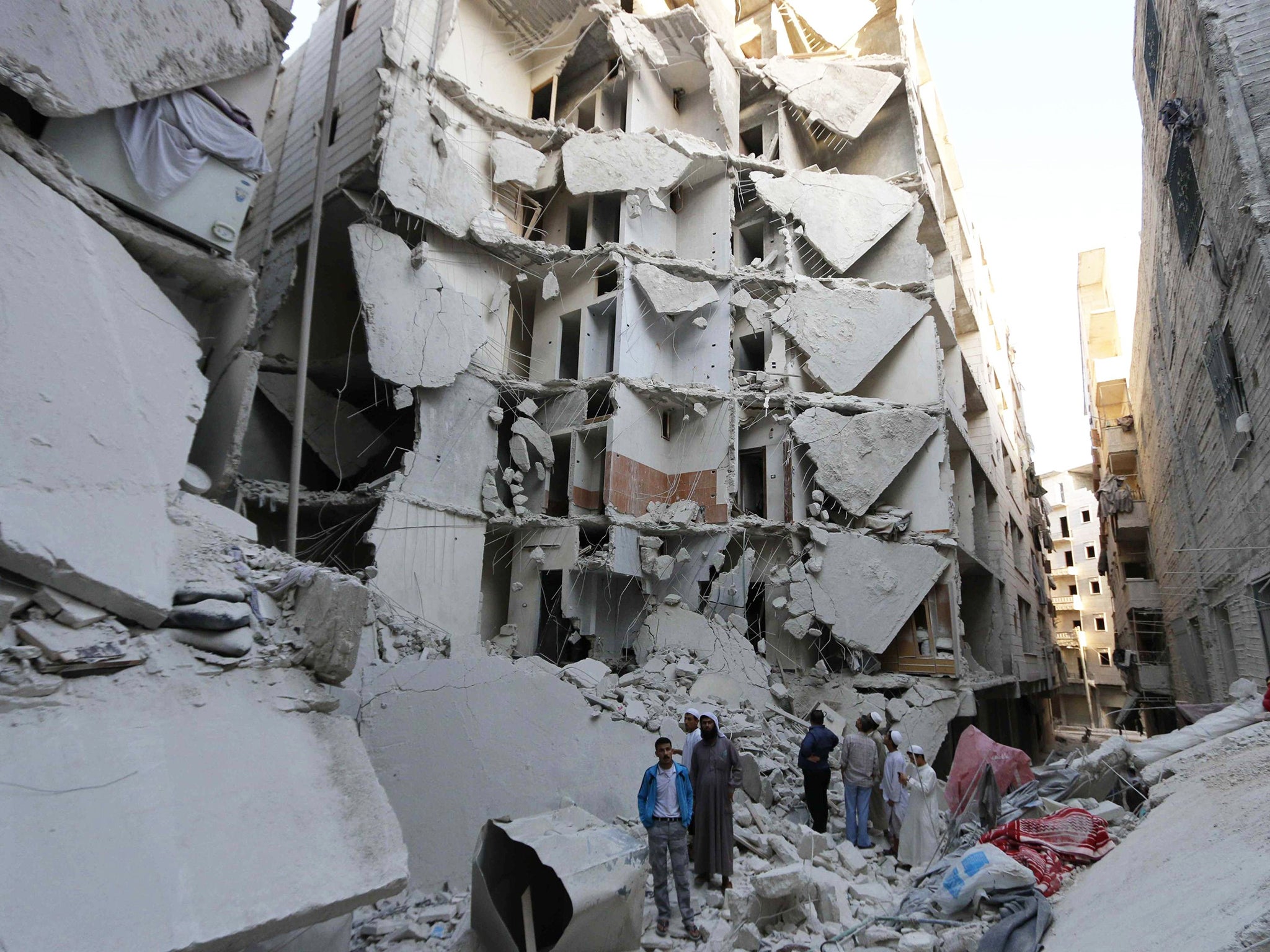 People stand on the rubble of collapsed buildings at a site hit by what activists said was a barrel bomb dropped by forces loyal to Syria's President Bashar al-Assad, in the Al-Fardous neighbourhood of Aleppo 