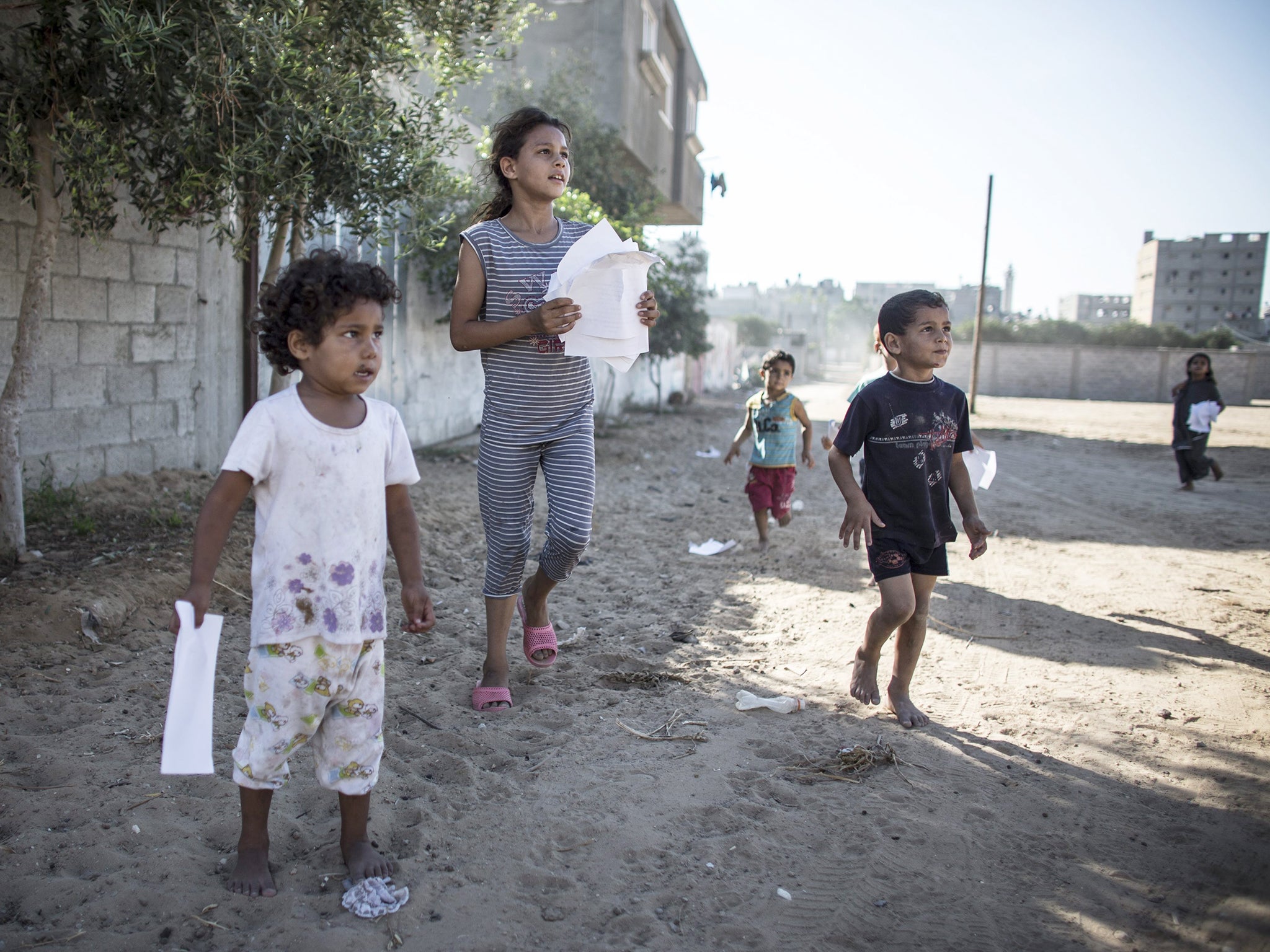Palestinian children run to collect leaflets dropped by Israeli Defense Forces over the Shuja'iyya neighbourhood in east Gaza City