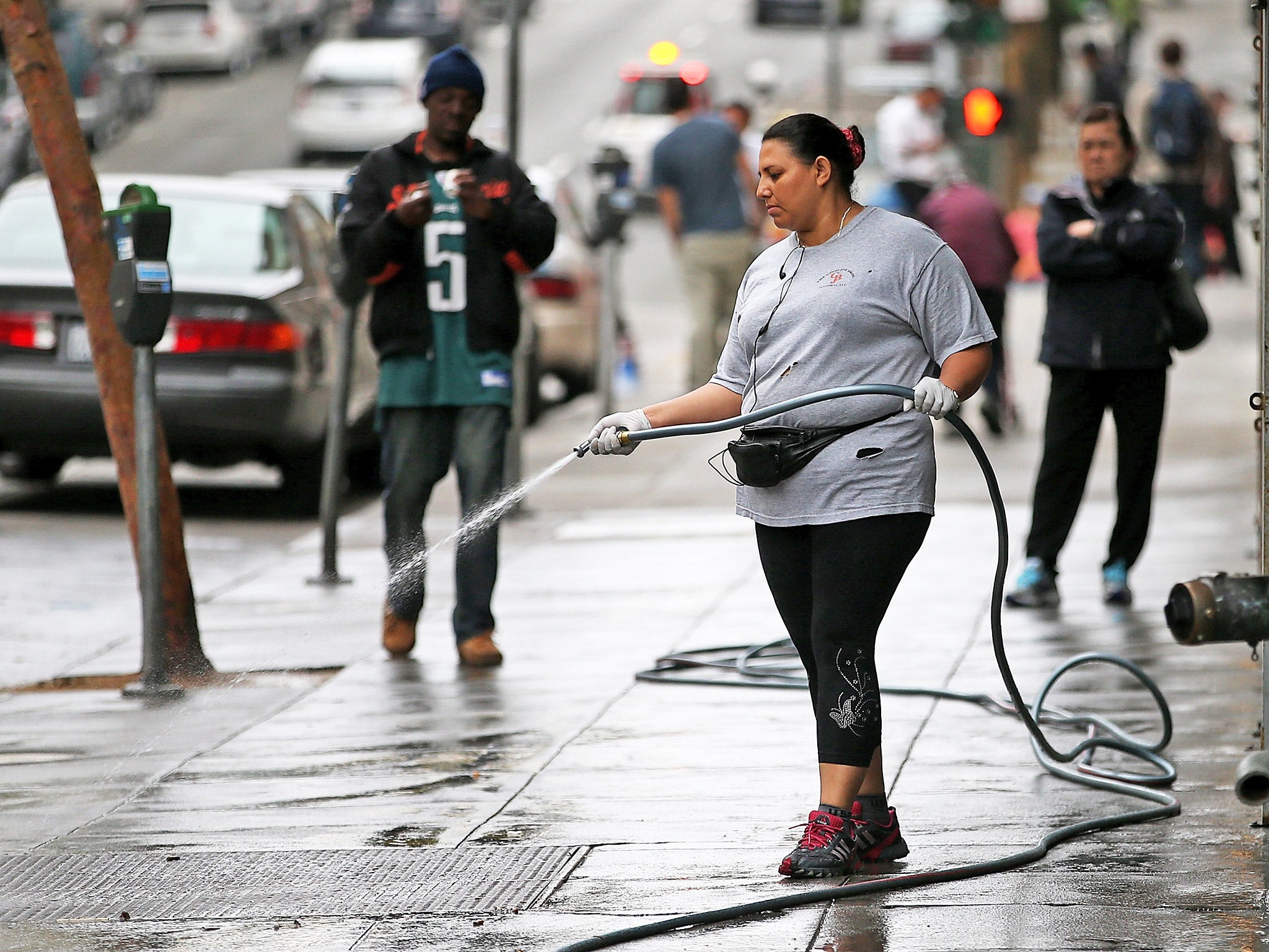 A woman uses a hose to wash the sidewalk in front of an apartment building in San Francisco, California