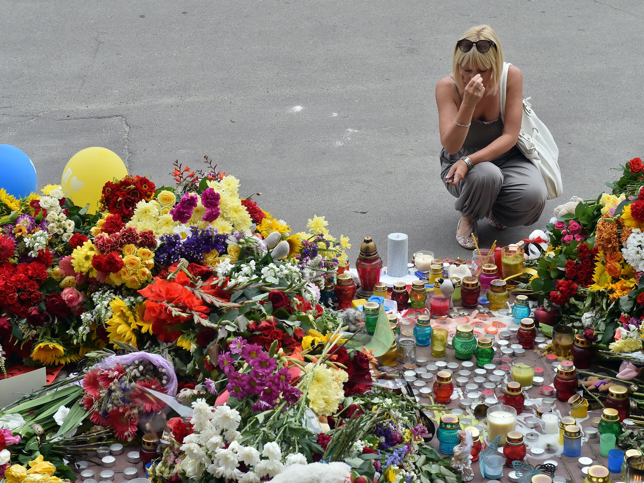 A woman crosses herself as people lay flowers and light candles in front of the Embassy of the Netherlands in Kiev, to commemorate passengers of Malaysian Airlines flight MH17 carrying 295 people from Amsterdam to Kuala Lumpur which crashed in eastern Ukr