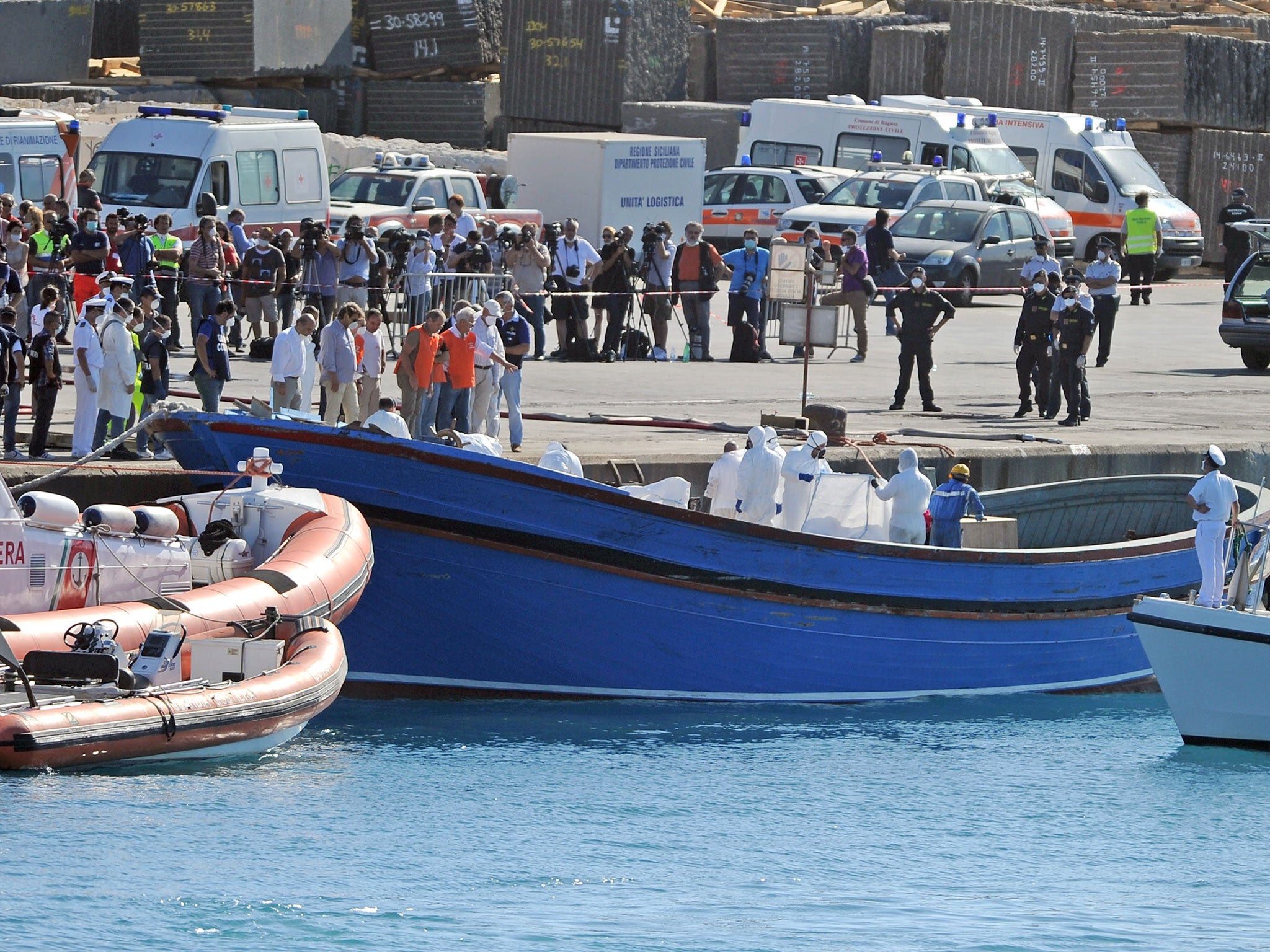 Firemen and policemen evacuate the dead bodies of migrants from a boat on July 1st, 2014 in the port of Pozzallo, Sicily, two days after a rescue operation off the coast. Rescuers found 45 victims stuffed into the hold of a fishing boat from north Africa