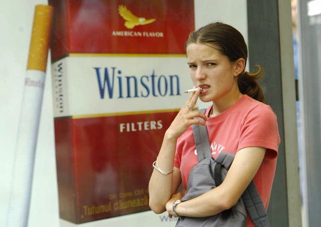 A young girl smokes near a commercial for cigarettes
