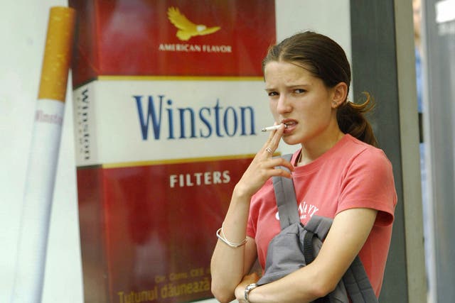 A young girl smokes near a commercial for cigarettes