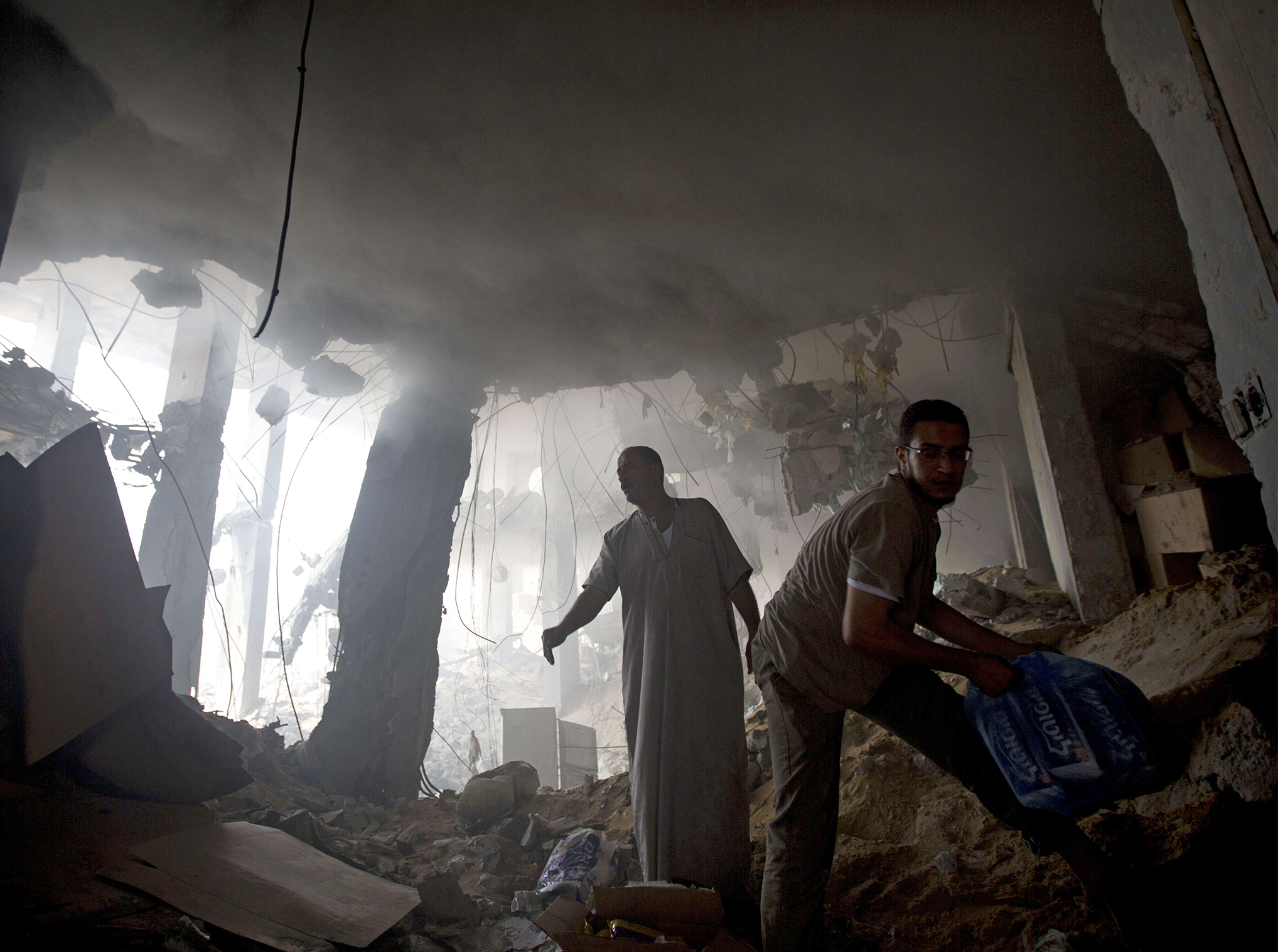 Palestinian men remove goods from the rubble of a destroyed store located on the ground floor of a building hit by an Israeli air strike