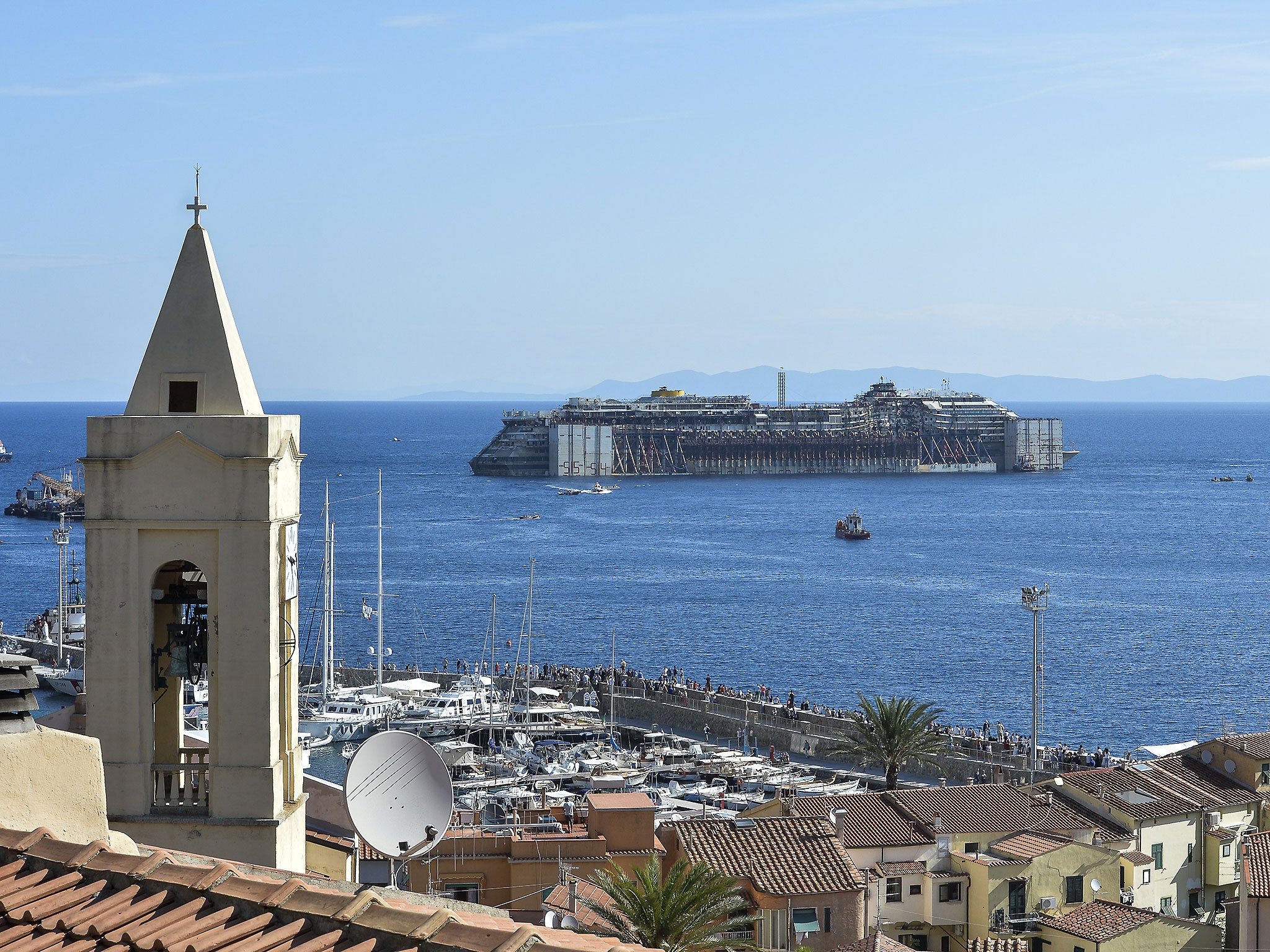 The wreck of the Costa Concordia is towed away from Giglio more than two-and-a-half-years after it sunk. In the foreground is the steeple of the church where many of the survivors were brought for refuge on 13 January 2012
