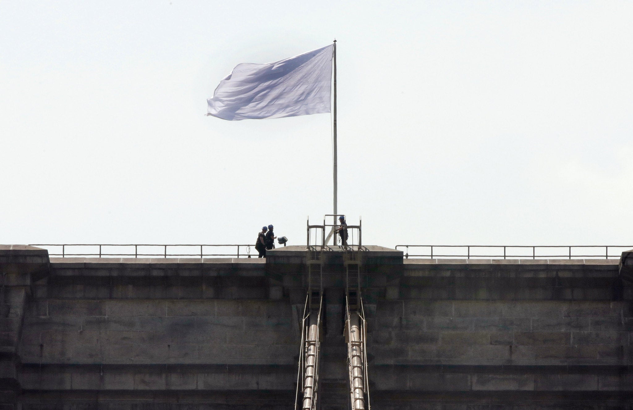 New York City Police officers stand at the base of a white flag flying atop the west tower of New York's Brooklyn Bridge, Tuesday, July 22, 2014. Someone replaced two American flags on the bridge with mysterious white flags. The white flags, international