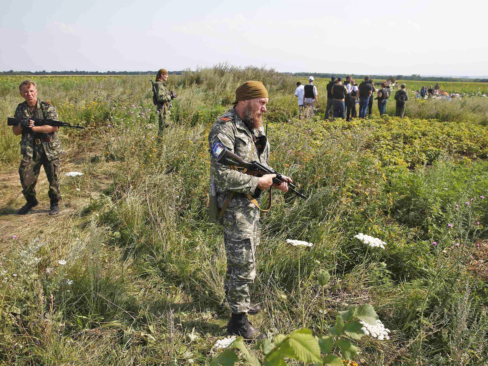 Armed pro-Russian separatists stand guard as monitors from the Organization for Security and Cooperation in Europe (OSCE) and members of a Malaysian air crash investigation team inspect the crash site of flight MH17