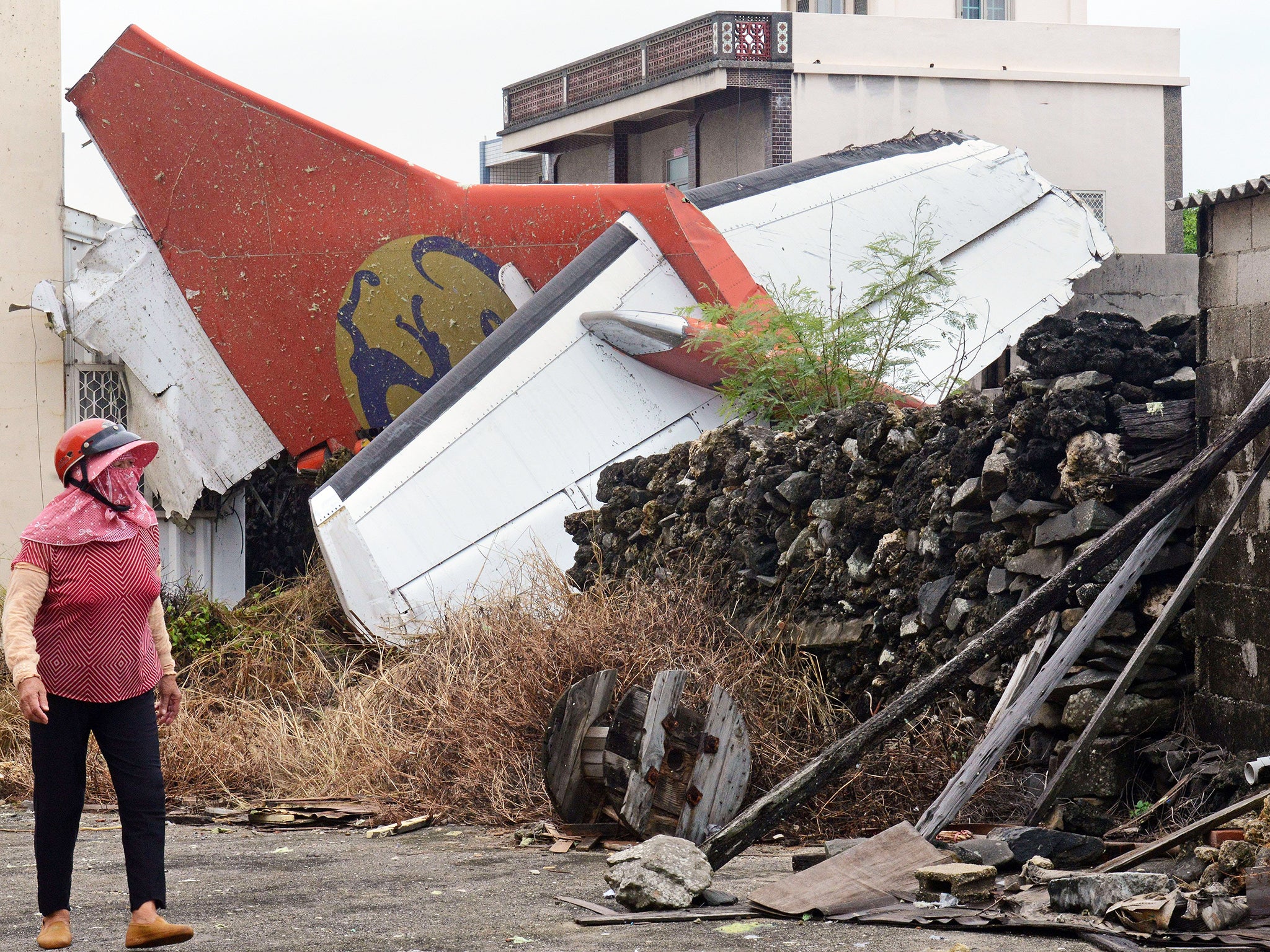 A local resident walks past the tail section of TransAsia Airways flight GE222 as rescue workers and firefighters search through the wreckage the morning after it crashed near the airport at Magong on the Penghu island chain
