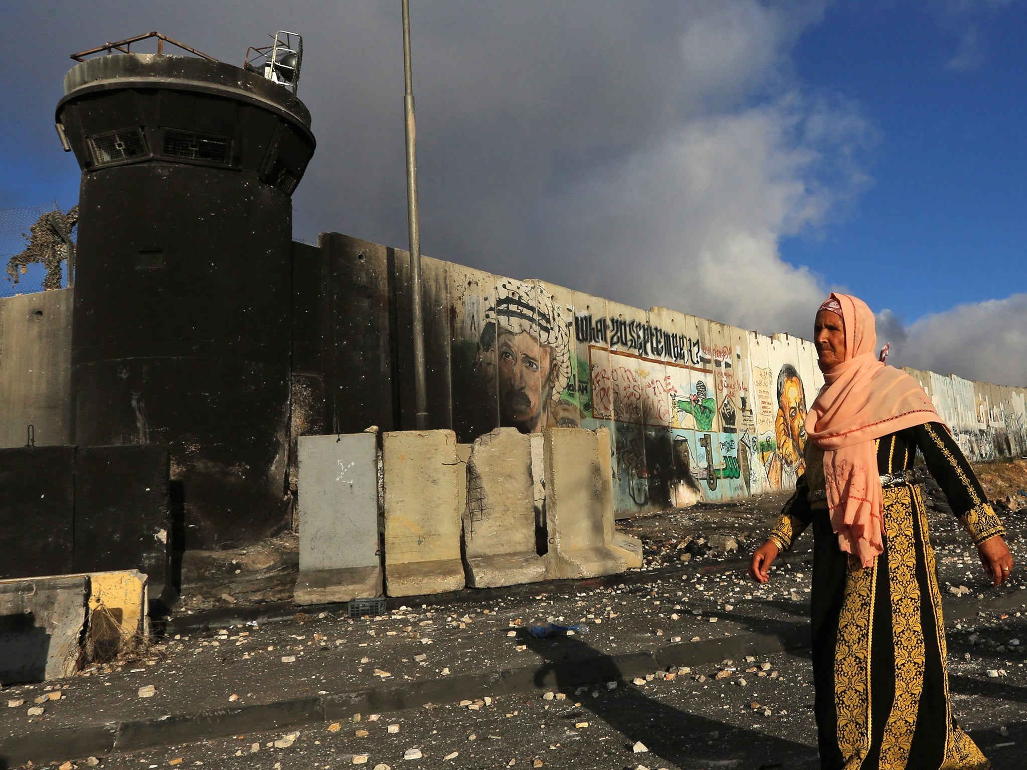 A Palestinian woman walks on the street full of stones which were hurled in clashes between Palestinians and Israeli security forces fill the street in front of an Israeli watch tower of the Qalandia checkpoint near the West Bank city of Ramallah