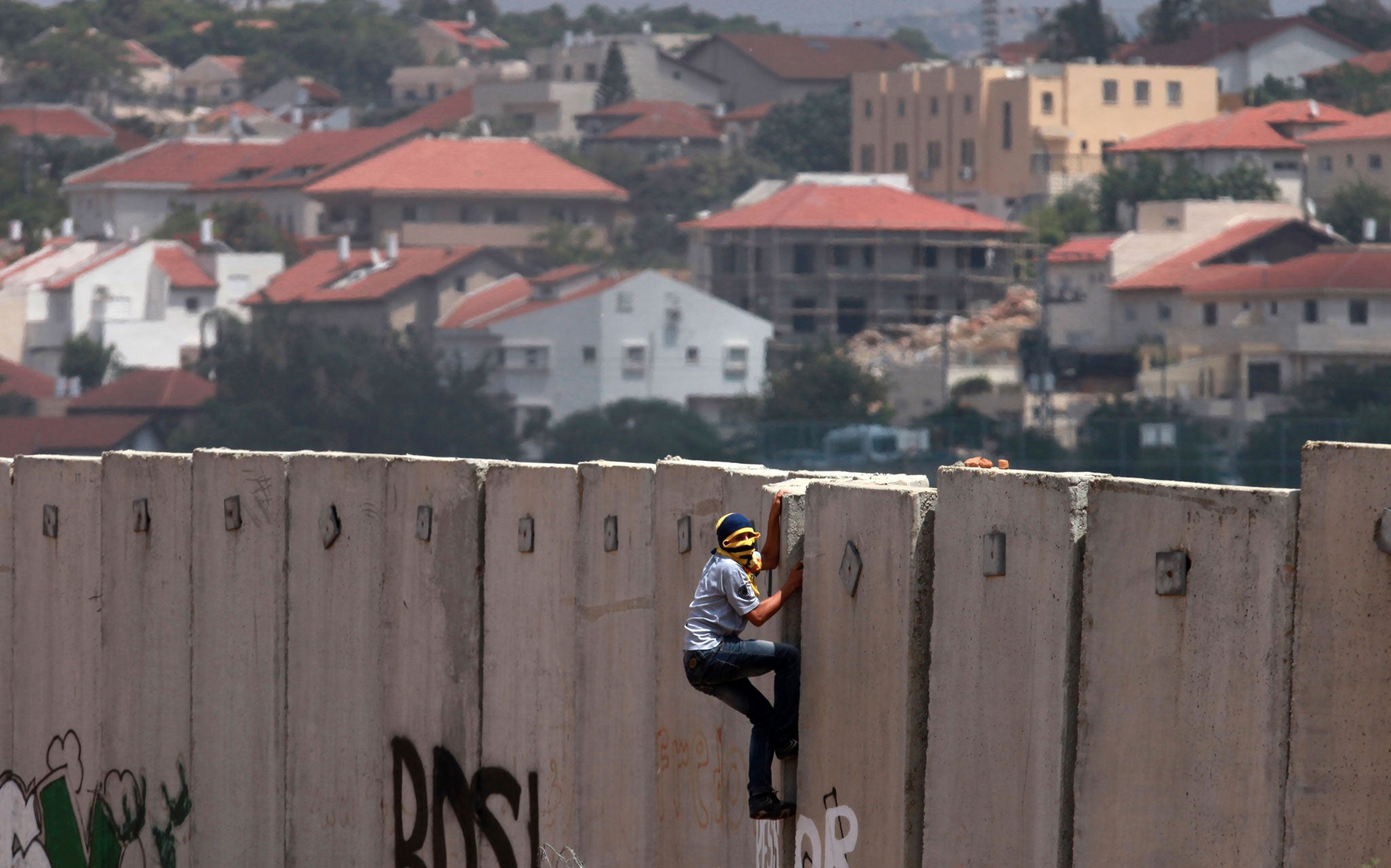A Palestinian protester climbs Israel's controversial separation barrier during clashes with Israeli security forces following a demonstration against Israeli settlements