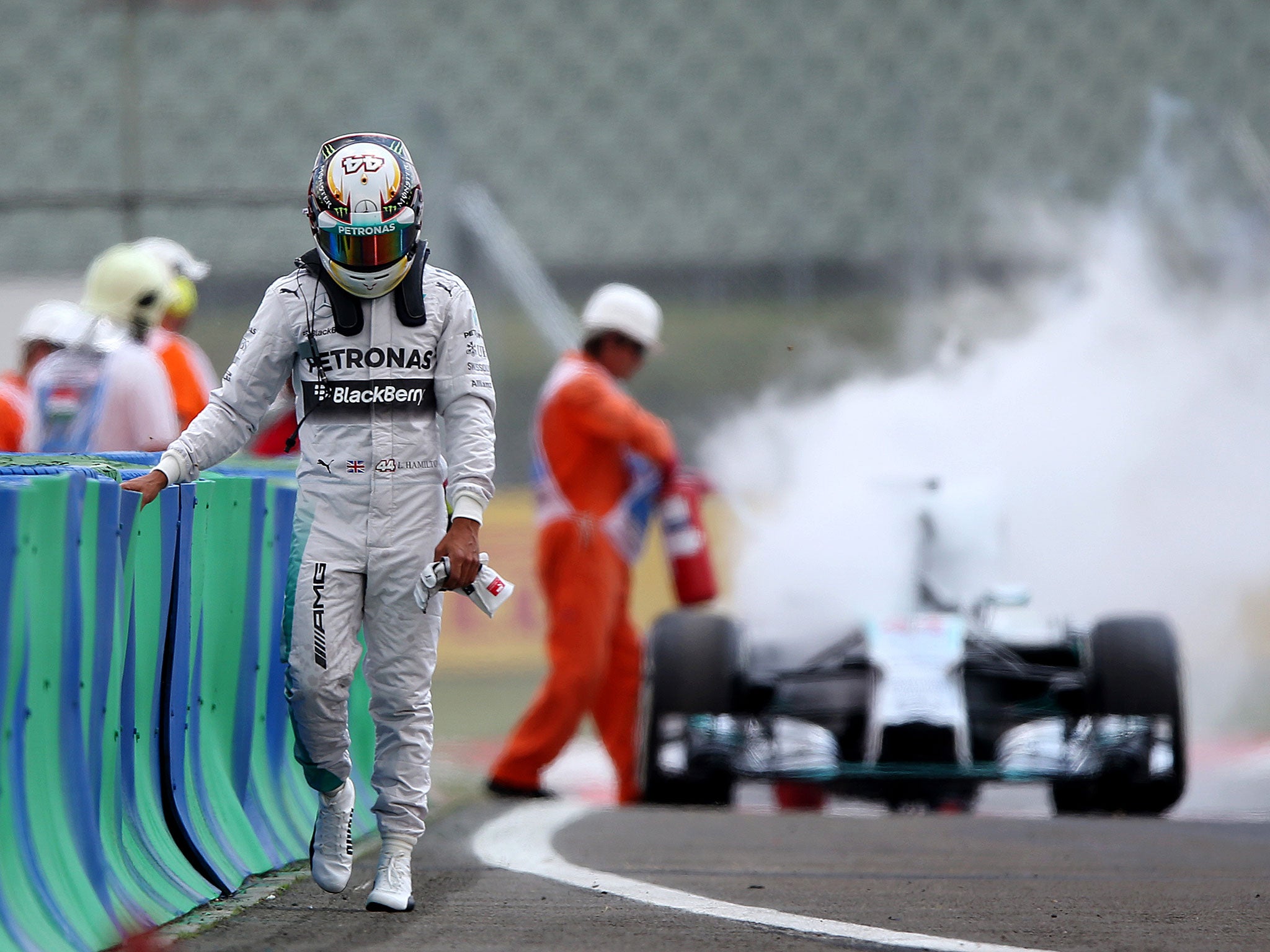 Lewis Hamilton walks back to the pit lane with his Mercedes burning in the background