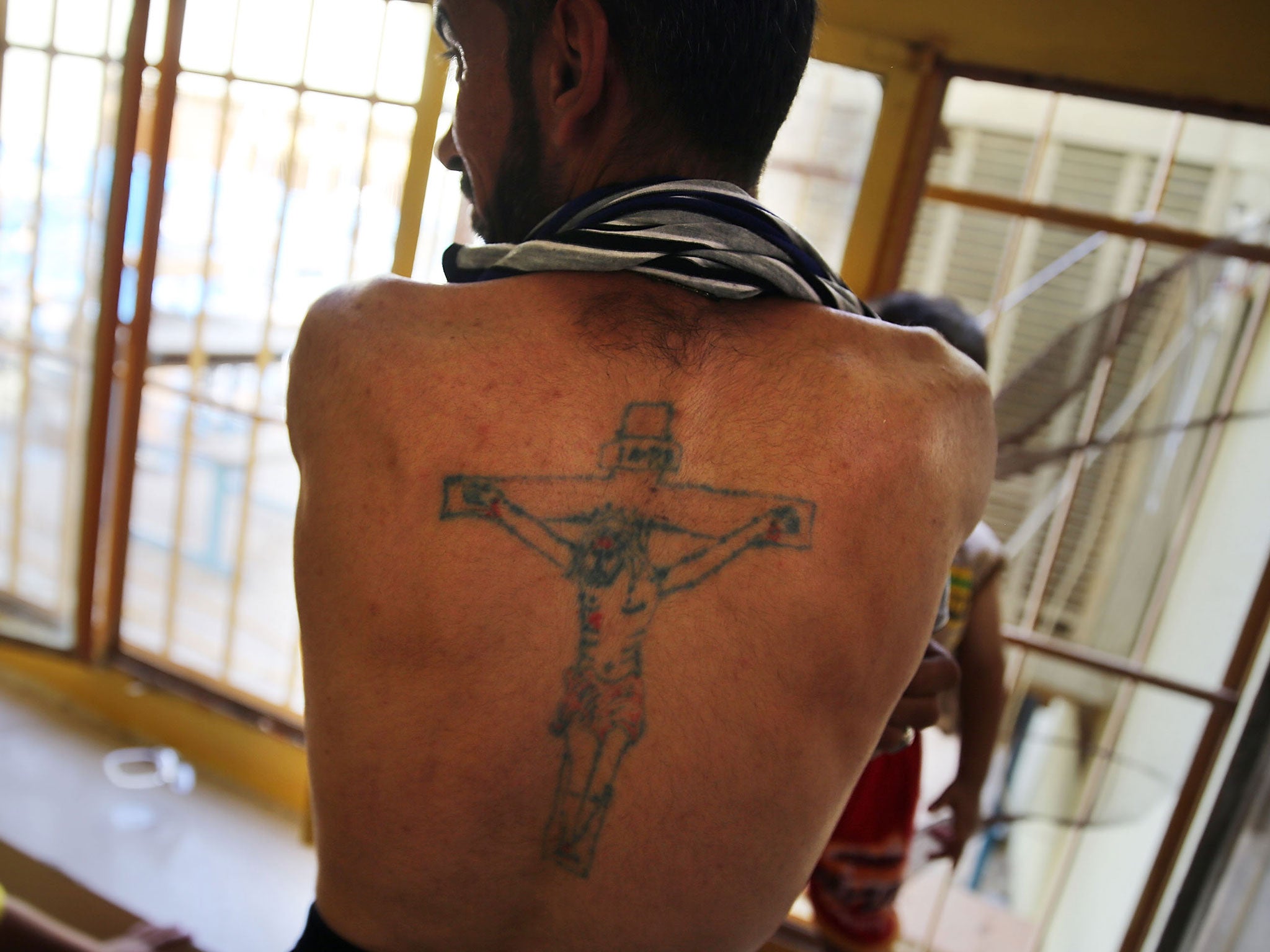 A displaced Iraqi Christian displays a tattoo of Christ on the Cross at Saint Joseph's church.