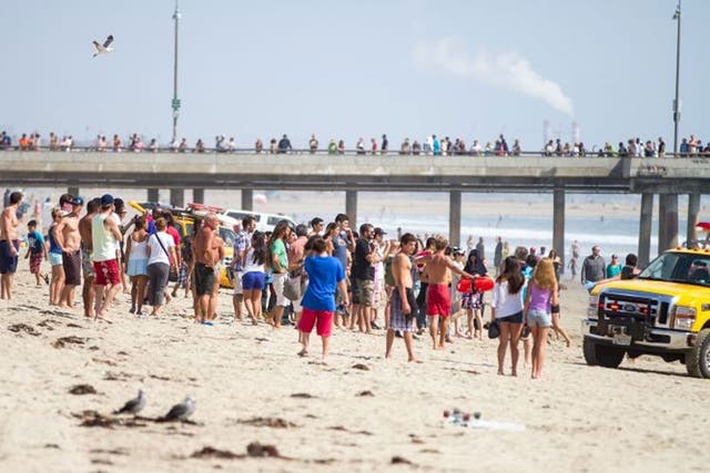 Pedestrians and beachgoers stand on the shore near Venice Beach as lifeguards, right, bring in a swimmer rescued from the water after a lightning strike Sunday July 27, 