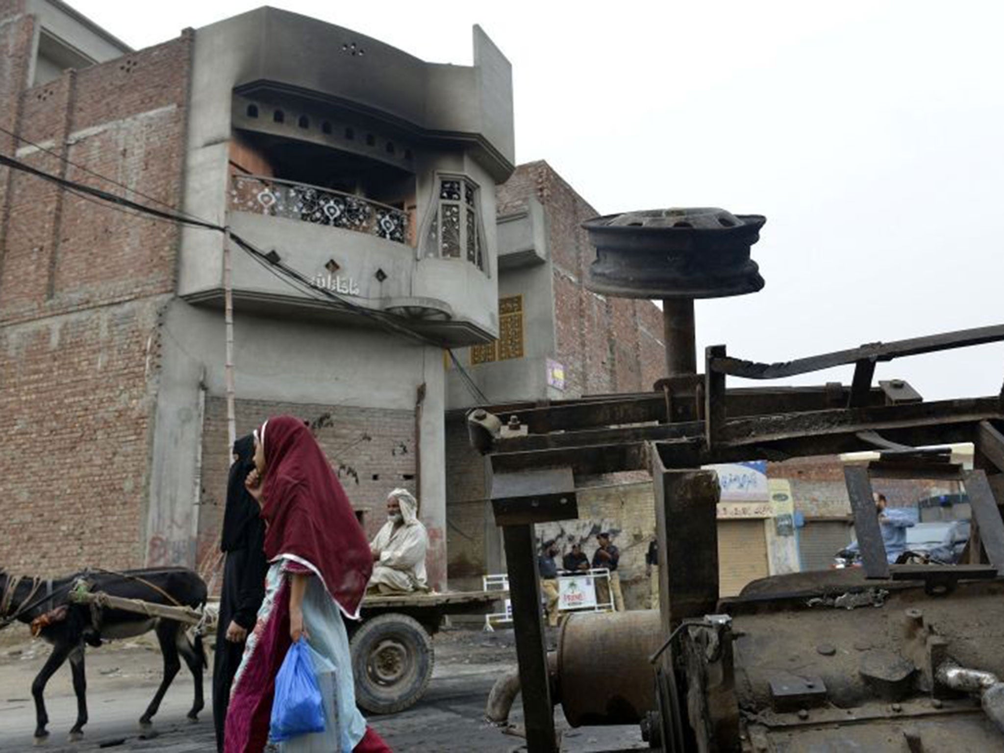 Pedestrians walks past the smoke-charred house of an Ahmadi resident following an attack by an angry mob in the low-income Arafat Colony