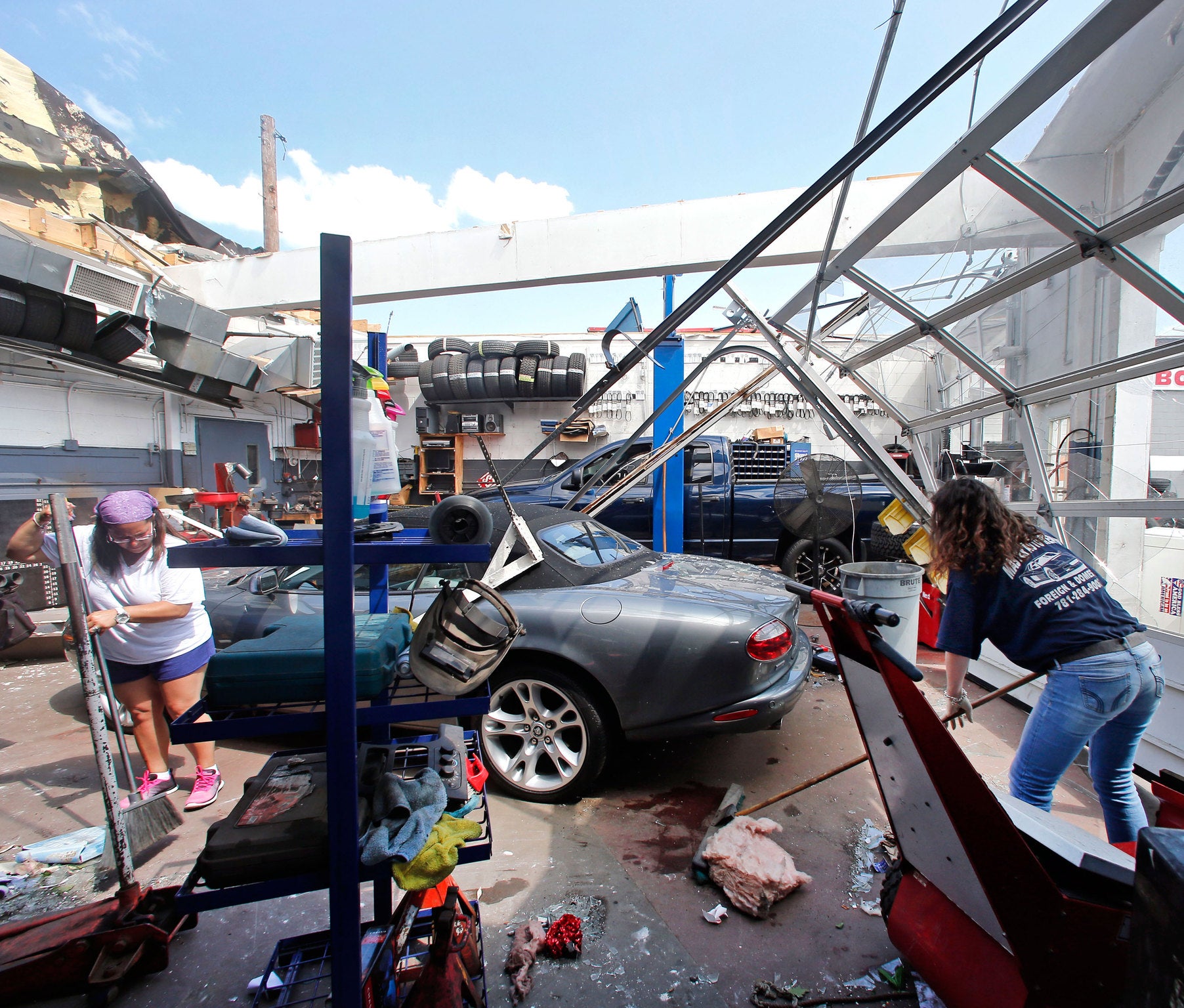 Master Auto manager Marie Annaloro, left, and Victoria Ohlson,right, sweep glass and debris in the service garage where the roof blew off in Revere, Mass