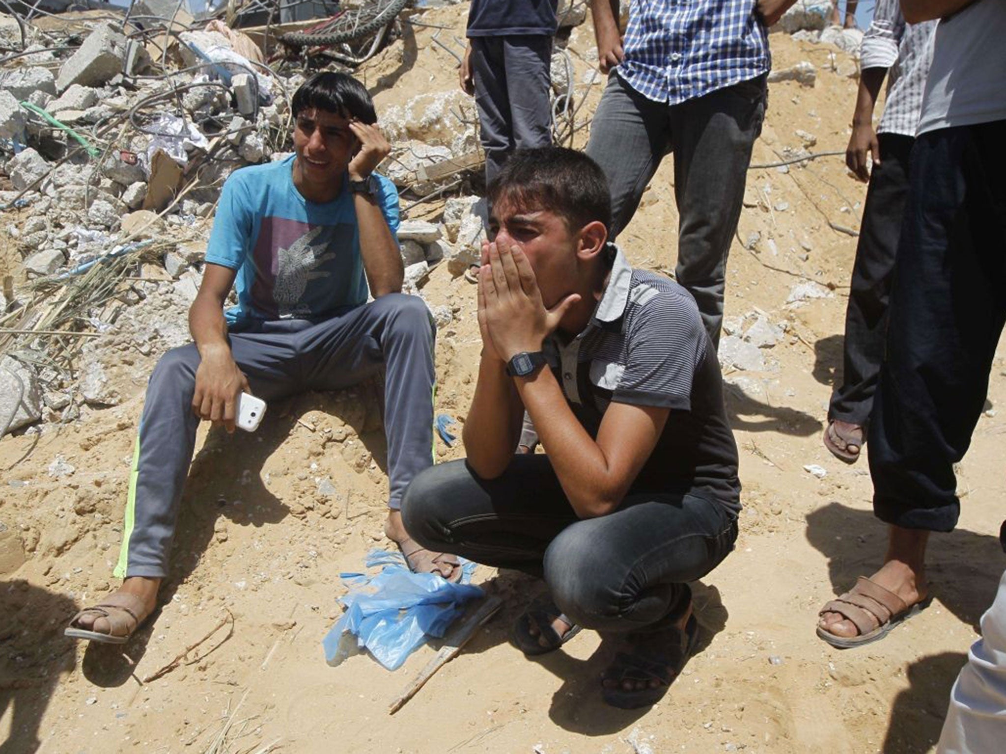 Palestinian youths weep as they watch rescue workers on July 30, 2014 removing the body of a dead child from under the rubble of the Duheir family home which was destroyed in an air strike