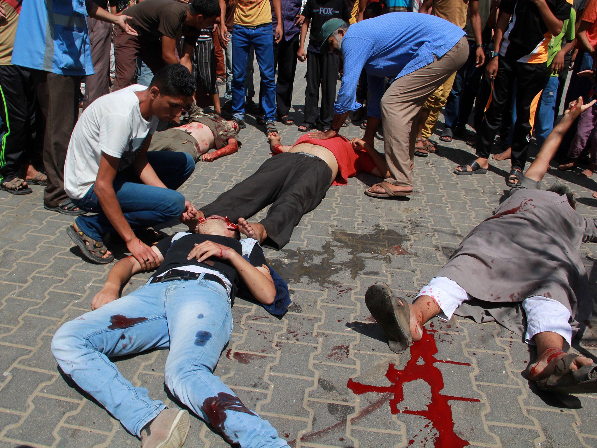 Palestinians aid injured people on the ground following an Israeli military strike on a UN school in Rafah on 3 August 2014