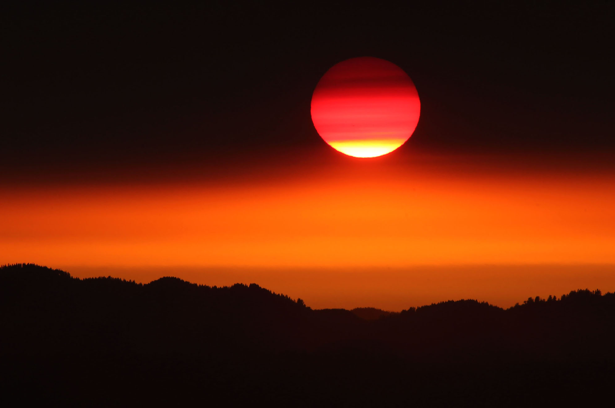 The Sun begins to peek out from below a layer of smoke blowing north from fires in southern Oregon and Northern California as it sets on the Willamette Valley near Eugene, Ore. (AP Photo/The Register-Guard, Chris Pietsch)
