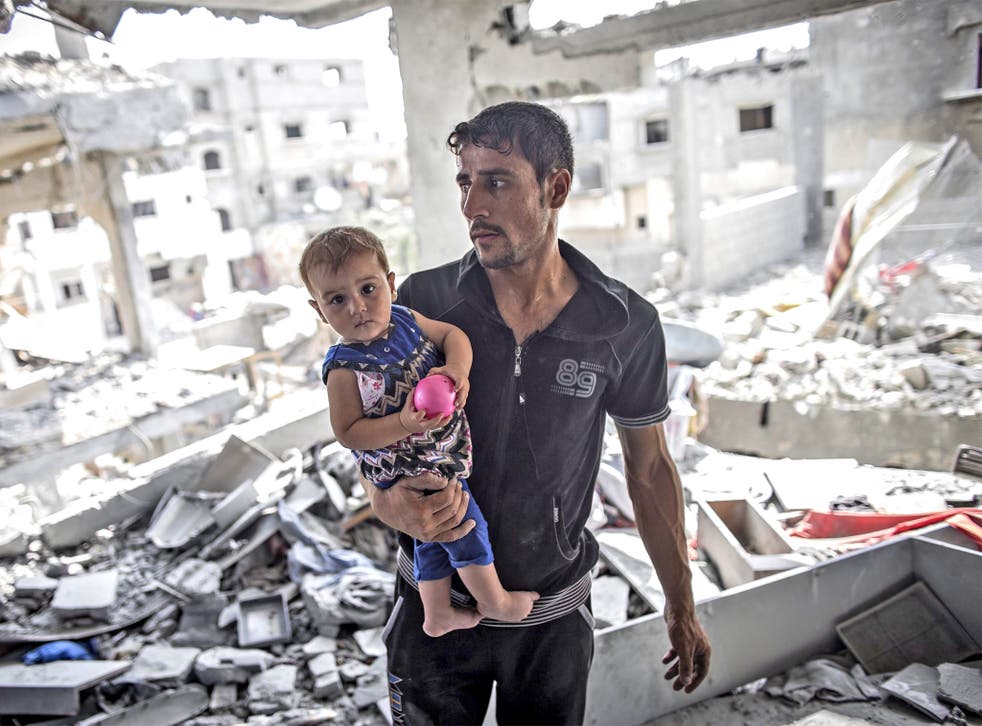 A Palestinian man holds his child in his destroyed home in Beit Hanoun