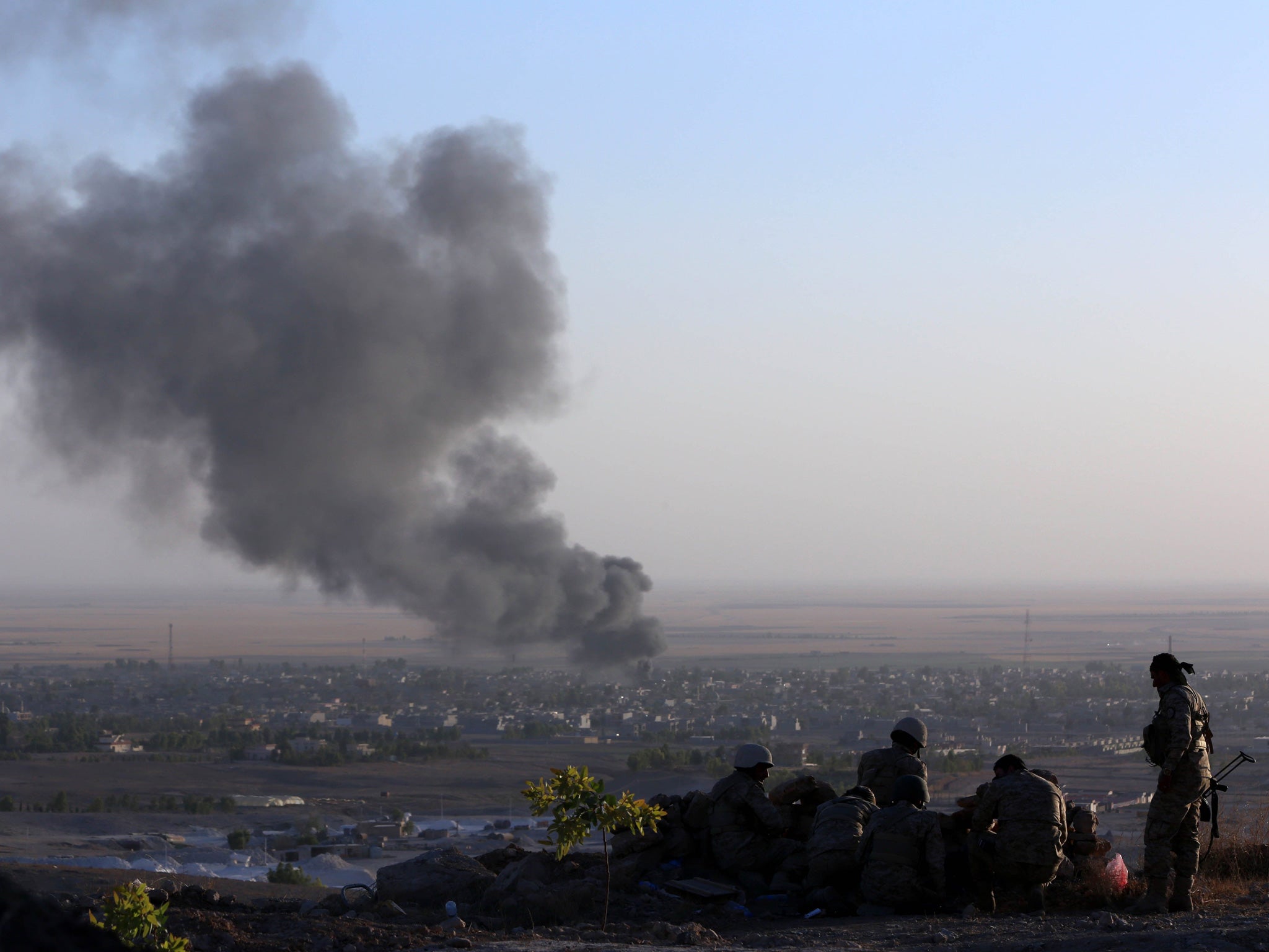 Iraqi Kurdish Peshmerga fighters look on as smoke billows from the town Makhmur, about 175 miles north of the capital Baghdad, during clashes with Isis militants