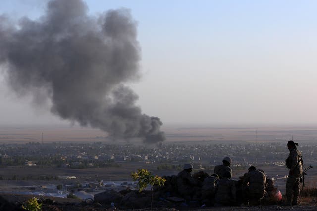 Iraqi Kurdish Peshmerga fighters look on as smoke billows from the town Makhmur, about 175 miles north of the capital Baghdad, during clashes with Isis militants