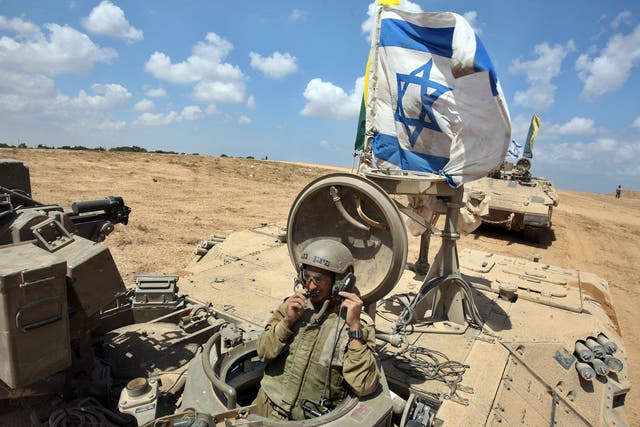 An Israeli soldier sits in an armored personnel carrier (APC) fyling the Israeli flag as they return from the border between Israel and the Gaza Strip