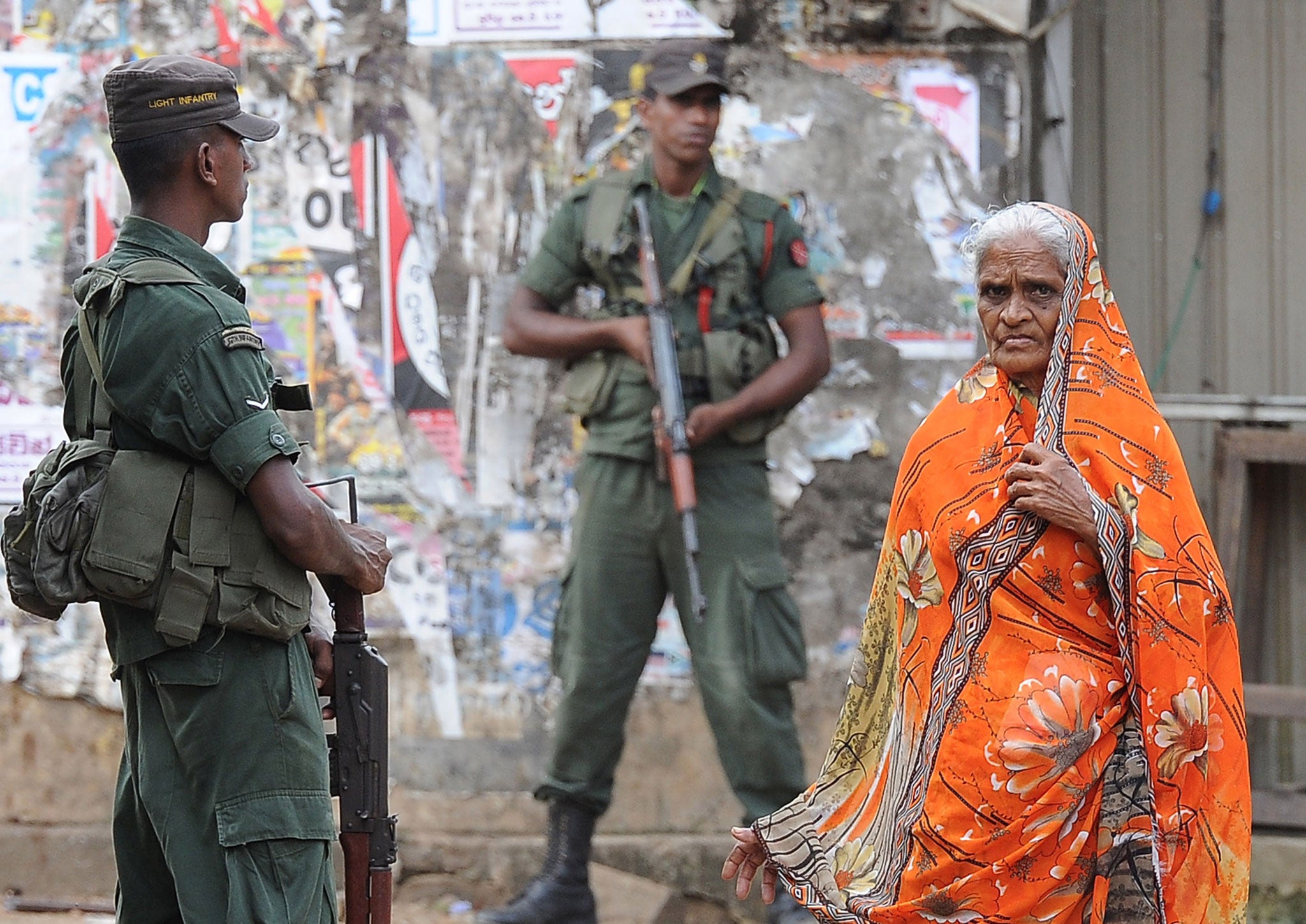 A Sri Lankan Muslim woman walks past soldiers following clashes between Muslims and an extremist Buddhist group in the town of Alutgama on June 17, 2014