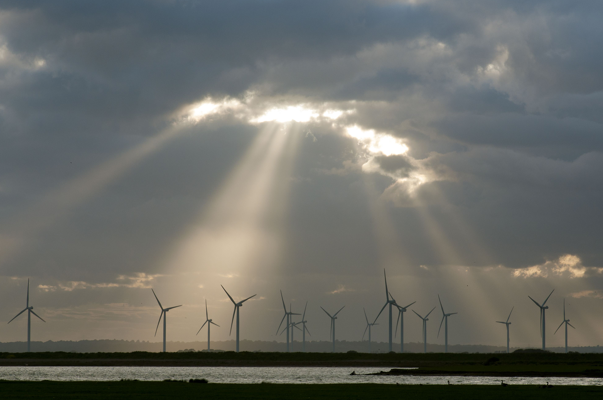 Wind turbines on windfarm with sunbeams through clouds at sunset, Little Cheyne Court, Romney Marsh, Kent