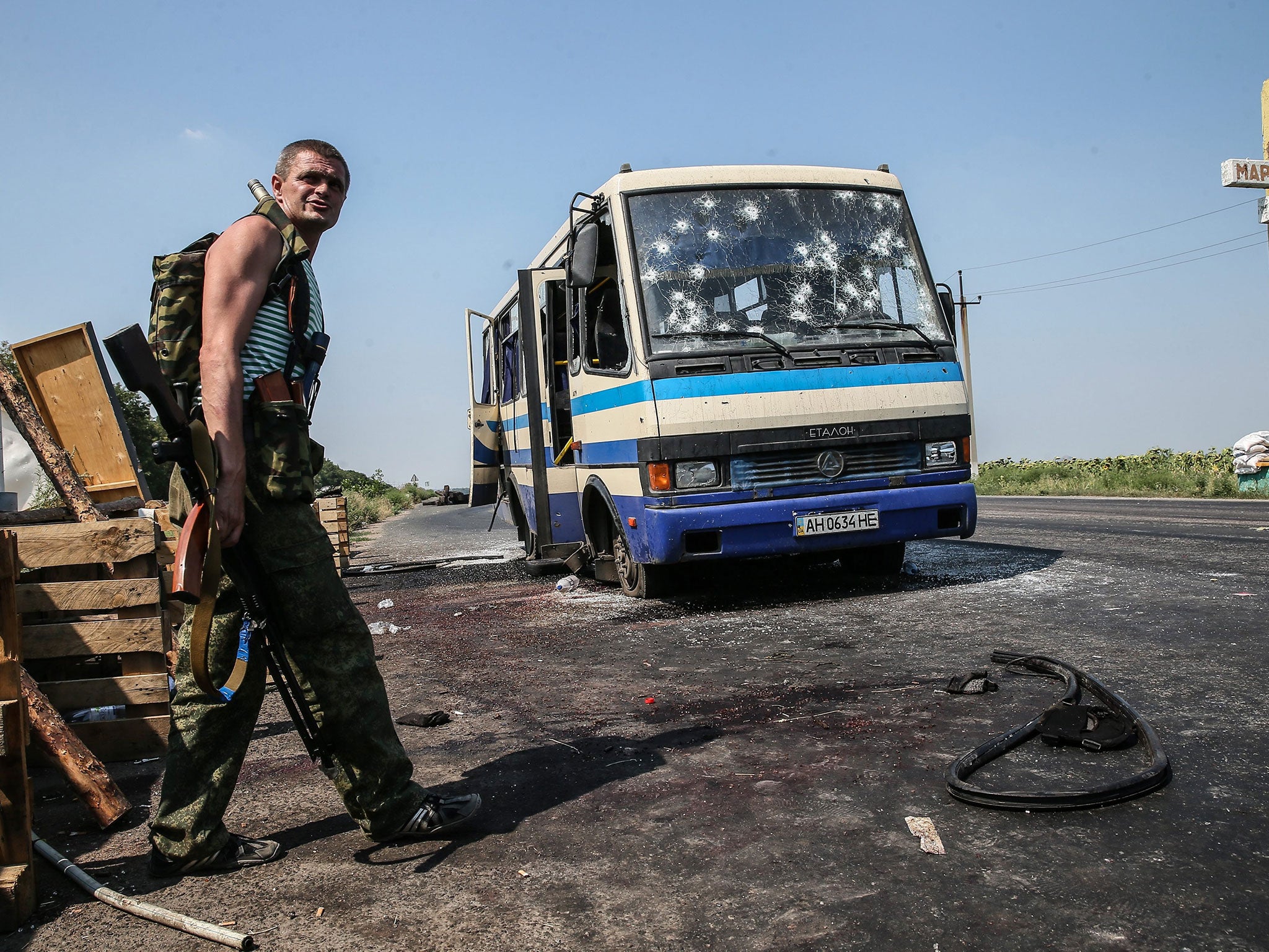 An armed pro-Russian separatist stands near the Ukrainian government-allied Right Sector’s bus that was ambushed in Donetsk yesterday. At least 12 people were killed in the attack