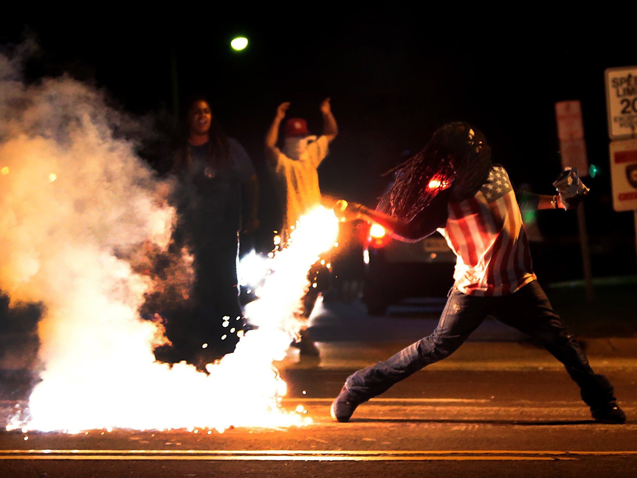 A demonstrator throws back a tear gas container after tactical officers worked to break up a group of bystanders on Chambers Road and West Florissant in St. Louis