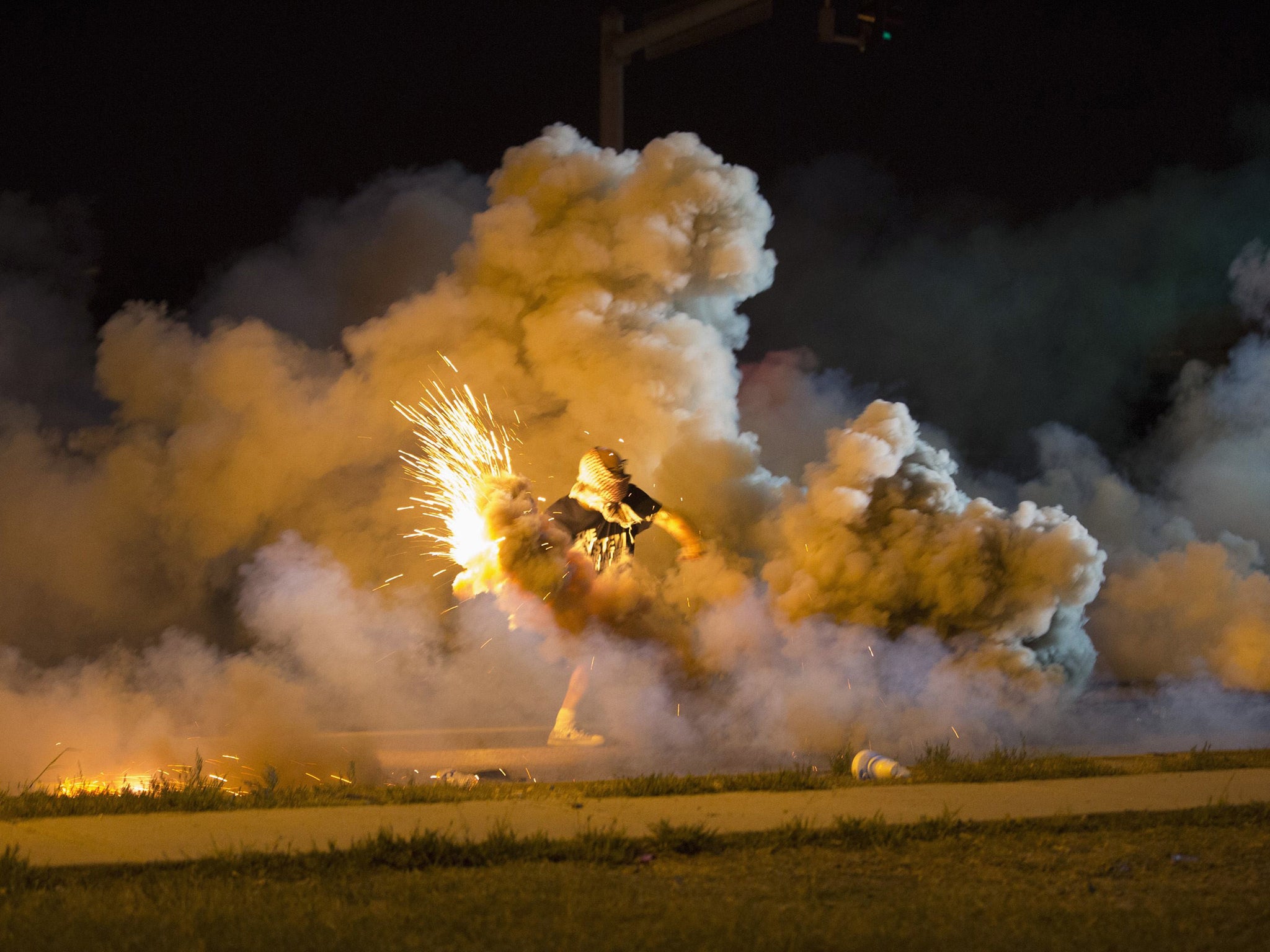 A protester throws back a smoke bomb while clashing with police in Ferguson