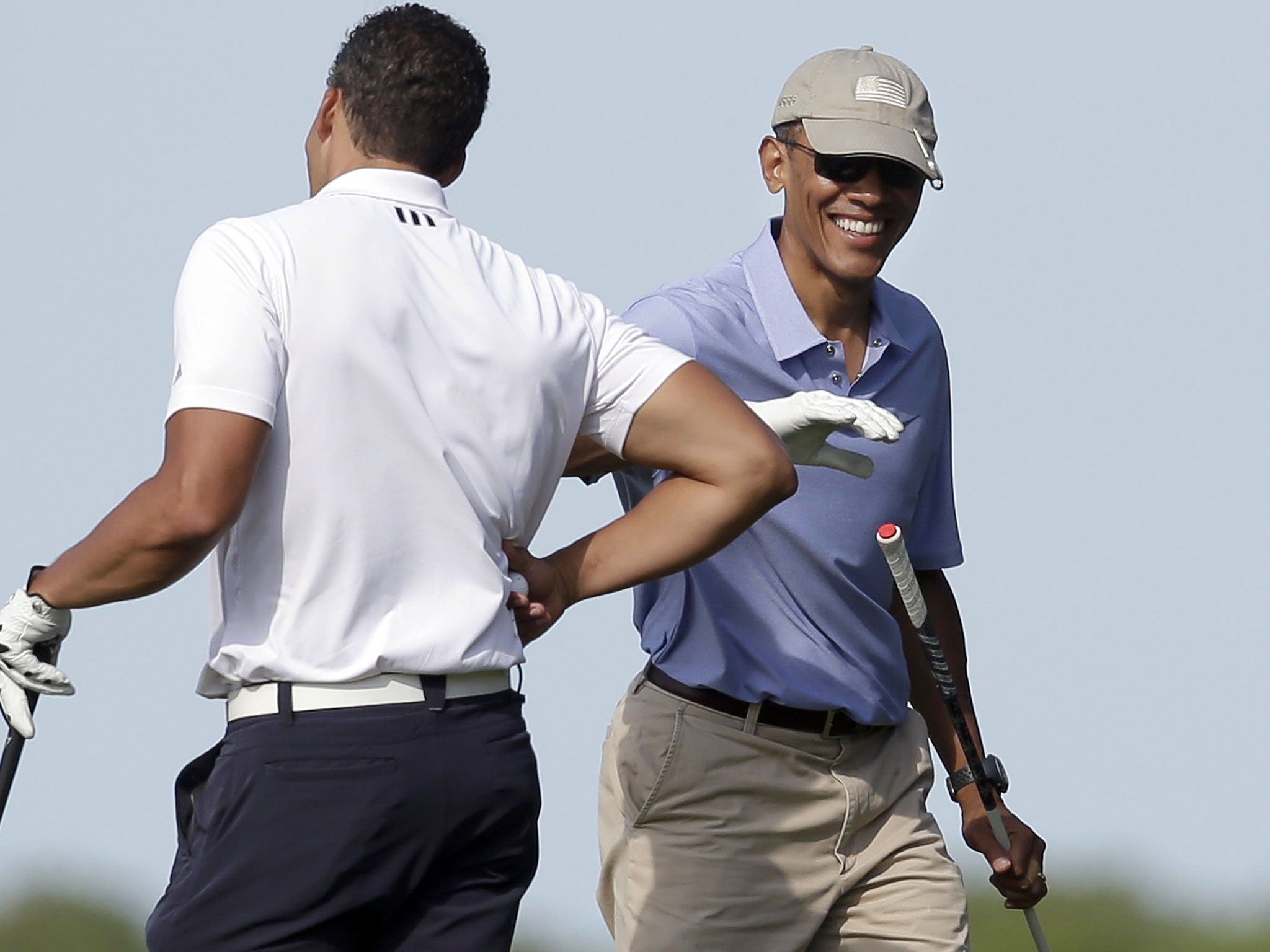 President Barack Obama, right, smiles as he gives a pat on the arm to Cyrus Walker, left, cousin of White House senior adviser Valerie Jarrett, while golfing at Vineyard Golf Club, Tuesday, Aug. 12, 2014, in Edgartown, Mass., on the island of Martha's Vin