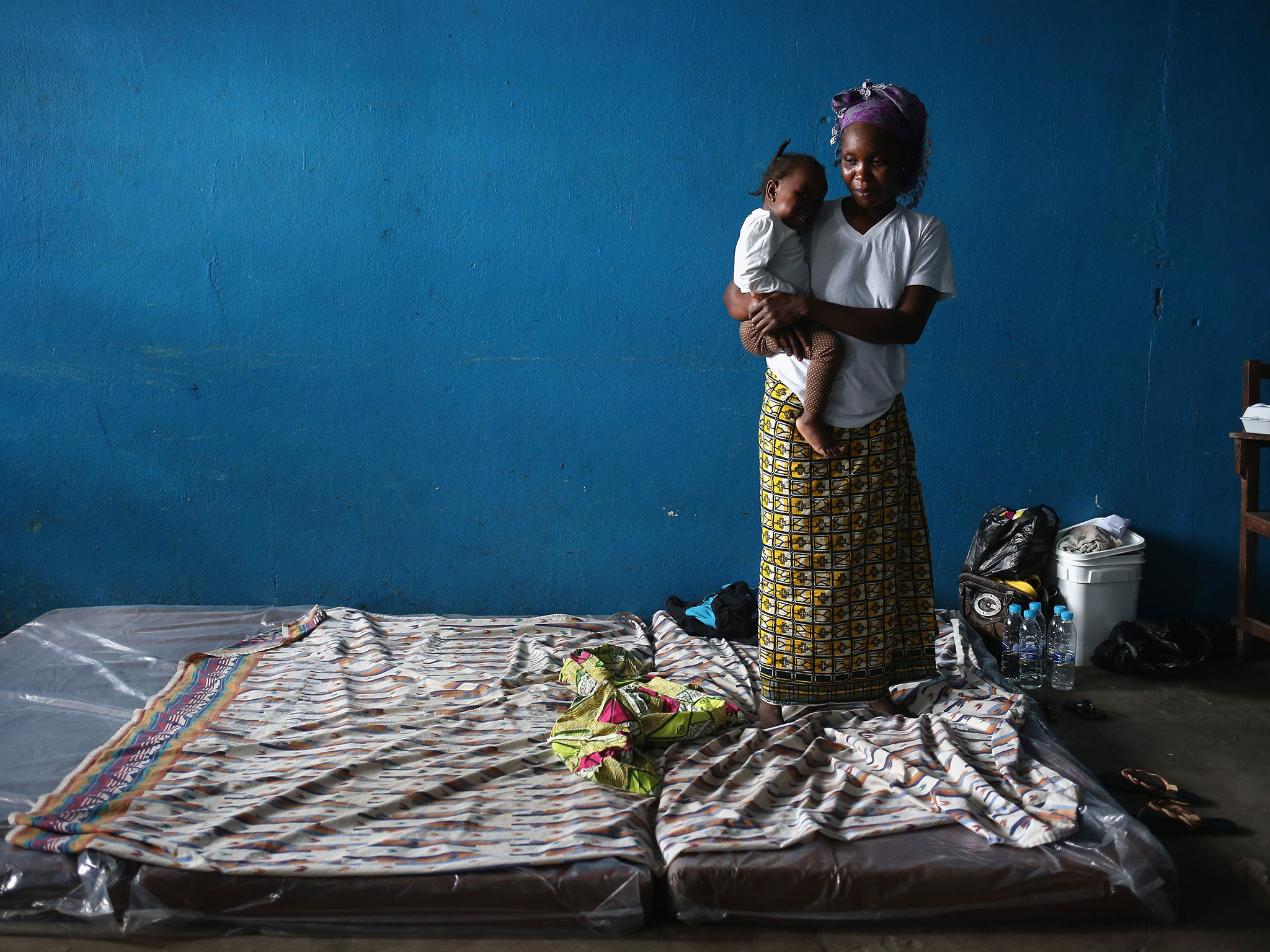 A mother and child stand atop their mattresses in a classroom now used as Ebola isolation ward