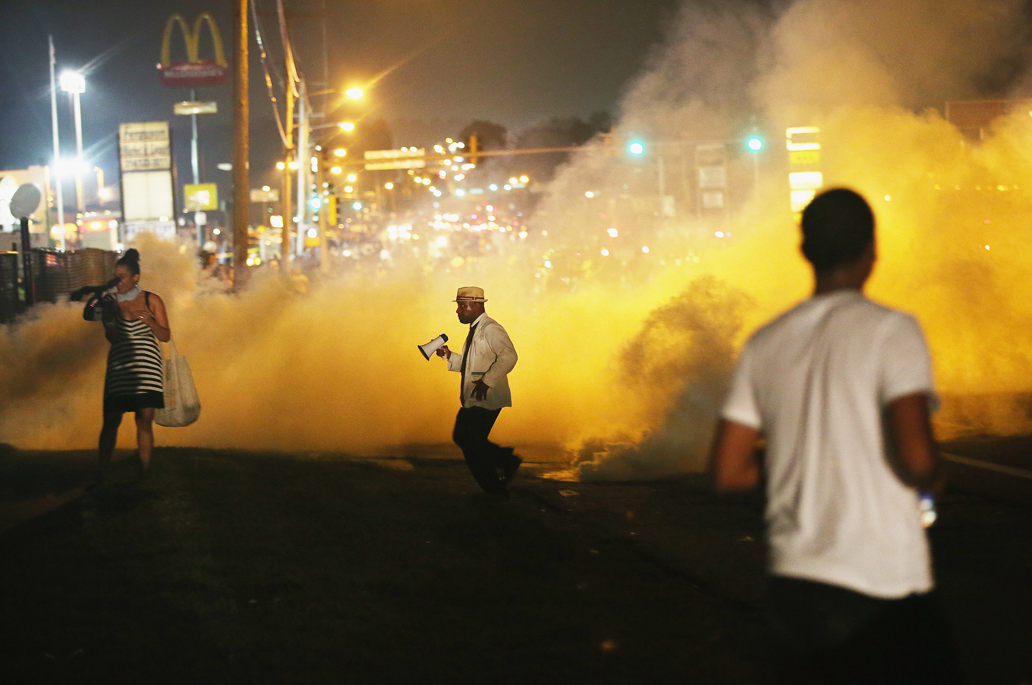 People make their way through the haze as tears gas fills the street during a demonstration over the fatal shooting of teenager Michael Brown by a police officer in Ferguson, Missouri