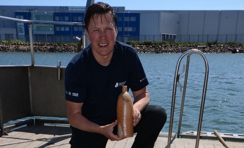 Underwater archaeologist Tomasz Bednarz holds the ancient bottle. Image: National Maritime Museum, Gdańsk