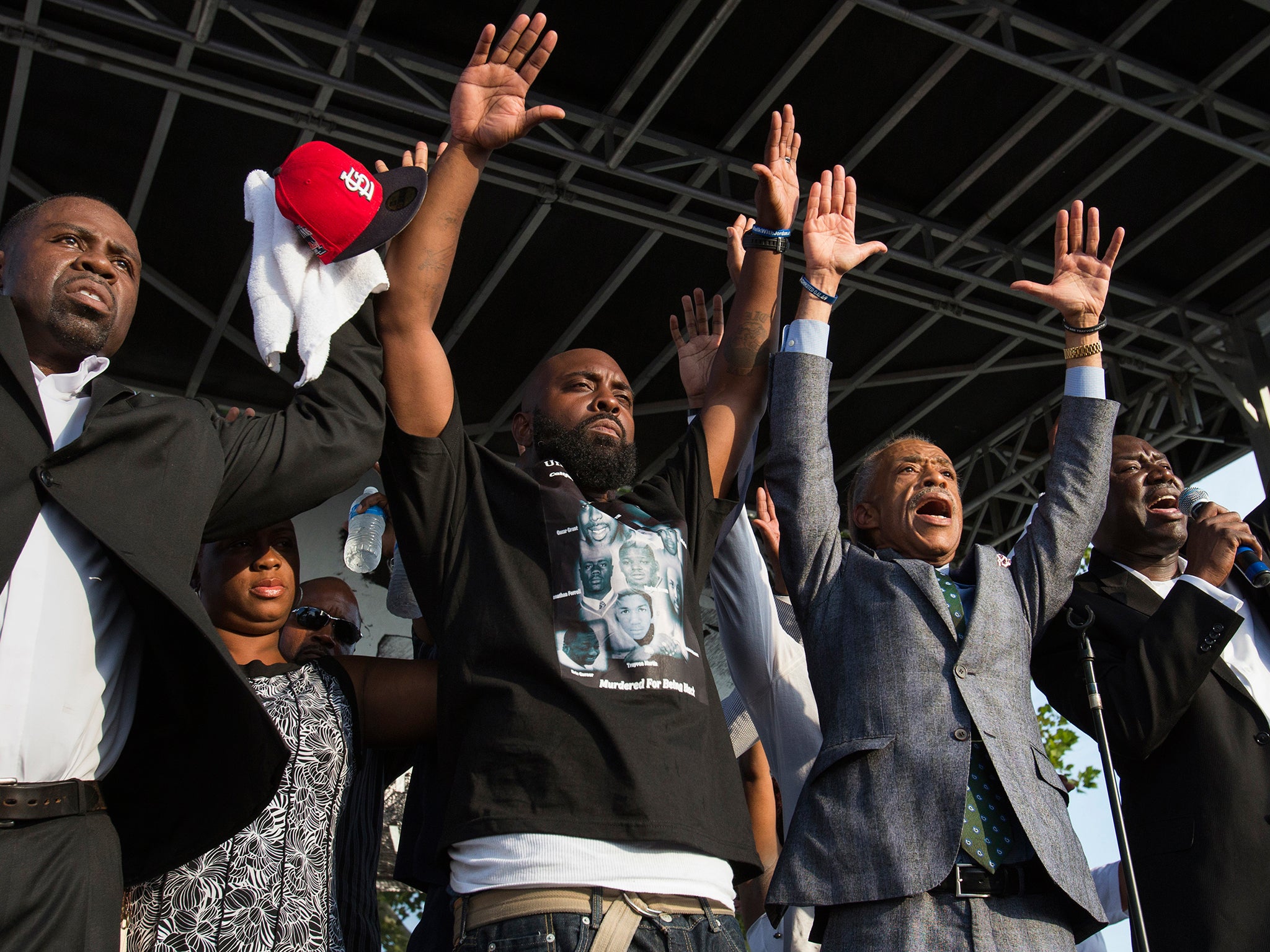 Michael Brown's parents raise their hands with Reverend Al Sharpton under the slogan, "Hands Up, Don't Shoot"