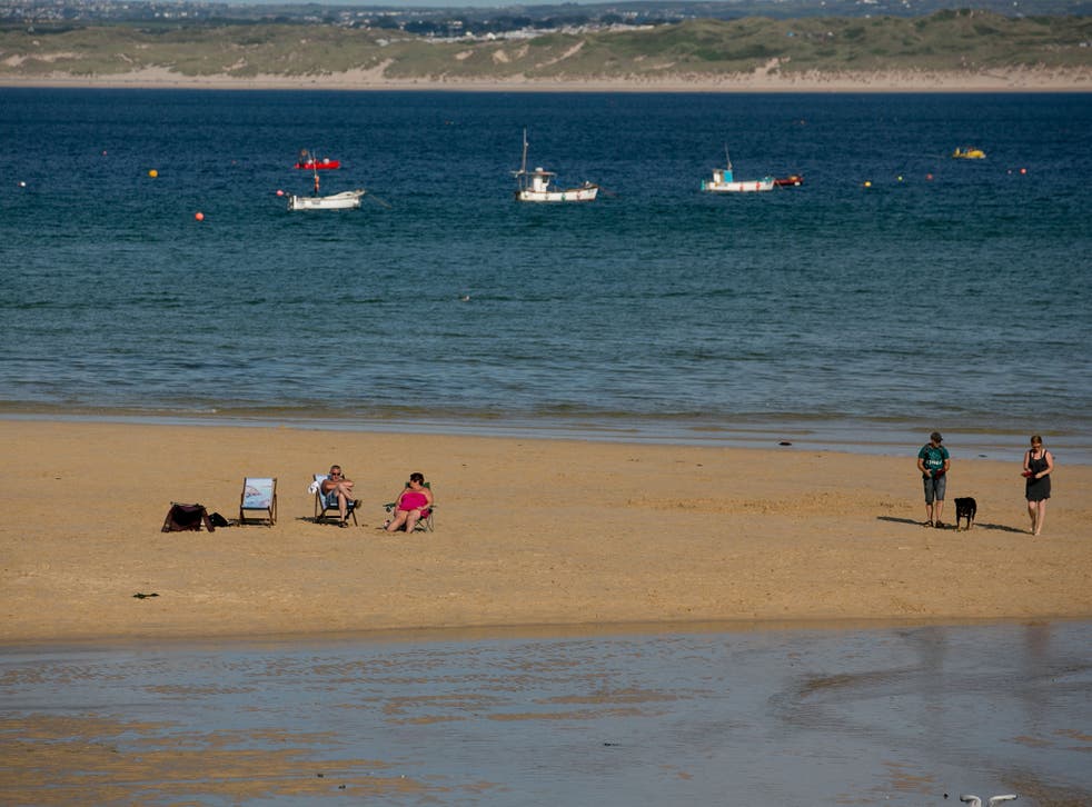 People sit on sand in the harbour at low tide in St Ives, Cornwall, England. 
