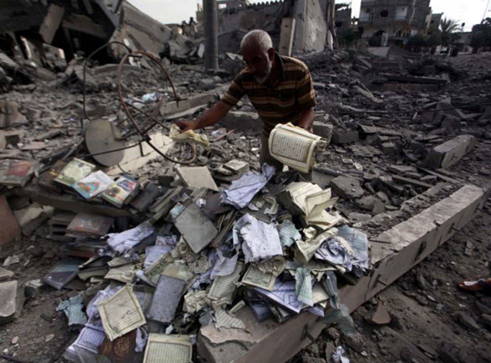 A Palestinian man collects copies of the Quran in the rubble of the Omar Ibn Abd al-Aziz mosque destroyed in an Israeli air strike in Beit Hanoun 