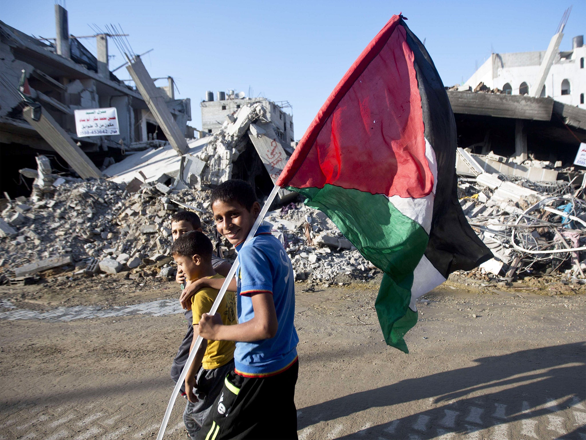 Palestinian children smile while walking through a scene of destruction