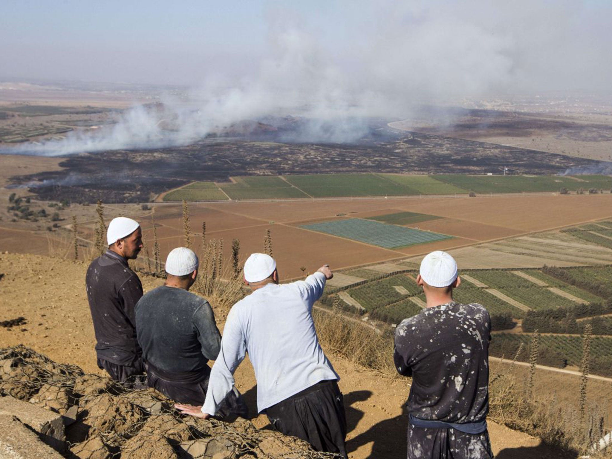 Druze men in the Golan Heights look on as smoke rises from the fighting between forces loyal to President Assad and rebels over the control of the Quneitra border crossing