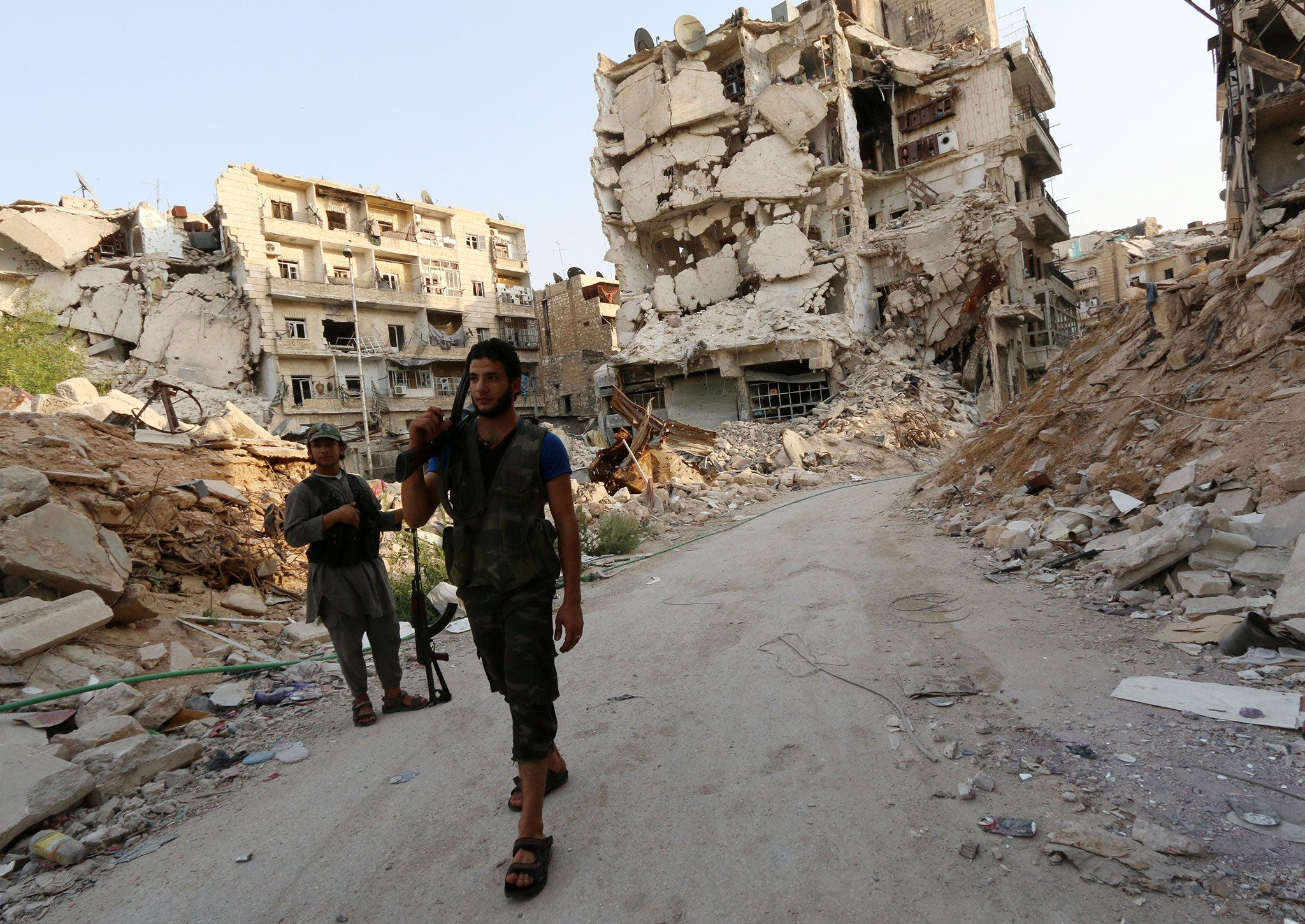 Rebel fighters walk in front of damaged buildings in Karam al-Jabal neighbourhood of Aleppo on August 26, 2014.