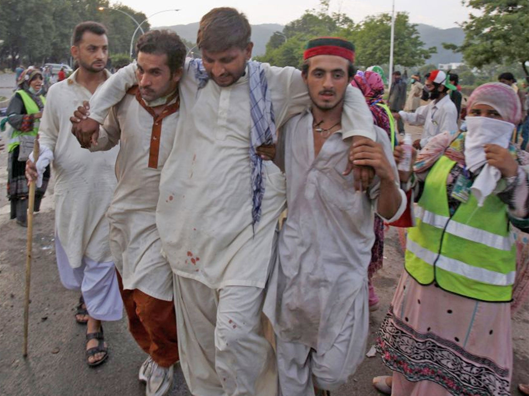 Pakistani protesters help carry their injured colleague to an ambulance during a clashes near prime minister's home in Islamabad, Pakistan