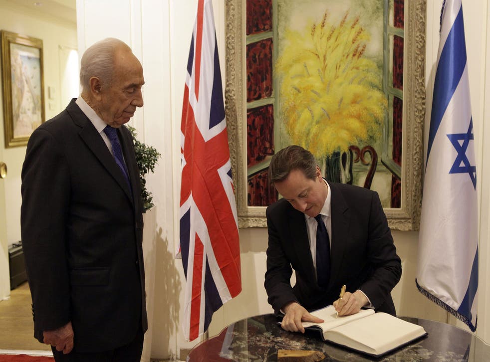 Israeli President Shimon Peres stands next British Prime Minister David Cameron as he signs the guestbook during a welcoming ceremony at the presidential compound in Jerusalem on March 12, 2014.